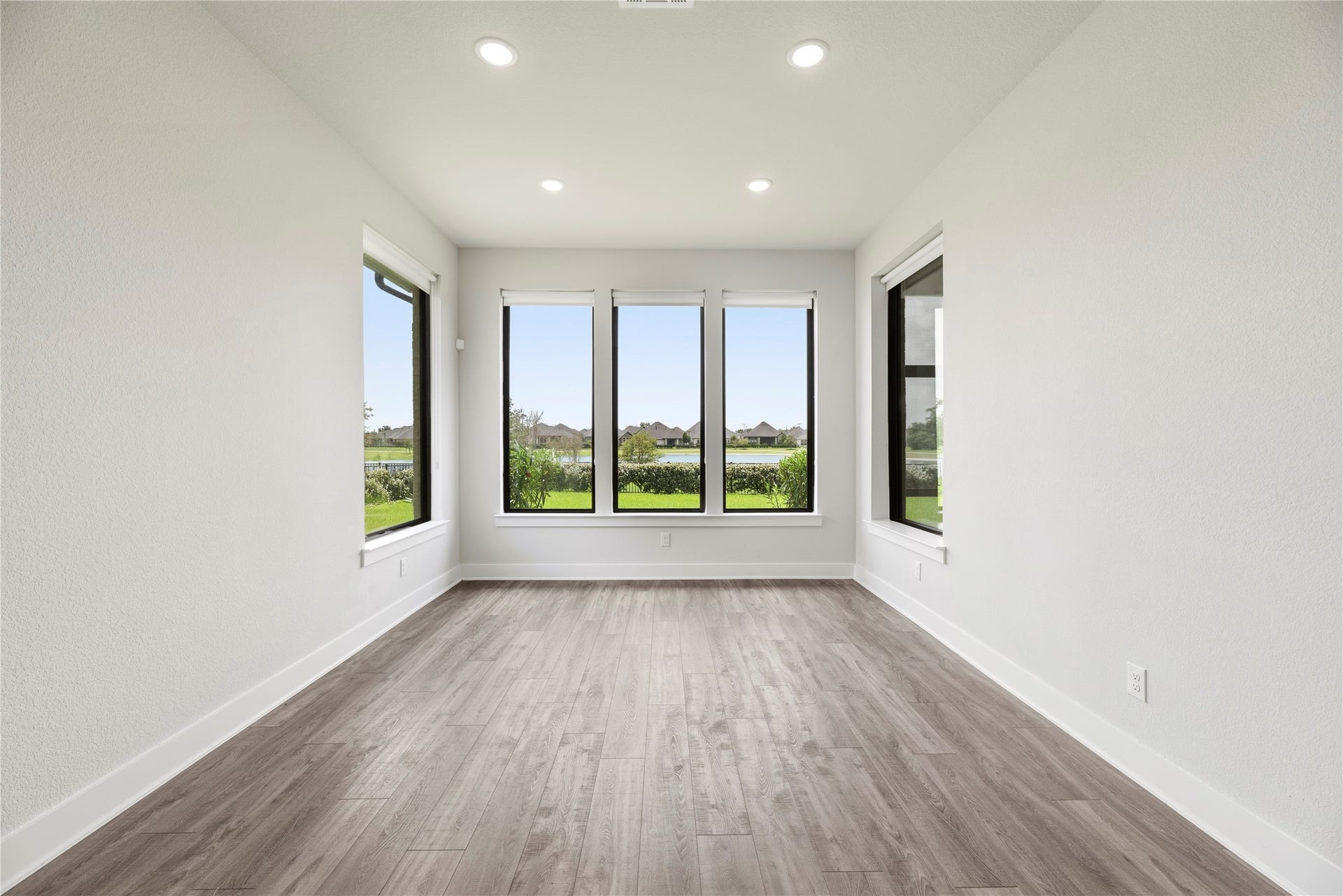 Versatile guest suite boasting warm wood-plank flooring, recessed lighting, and panoramic views of the neighborhood lake through large picture windows.