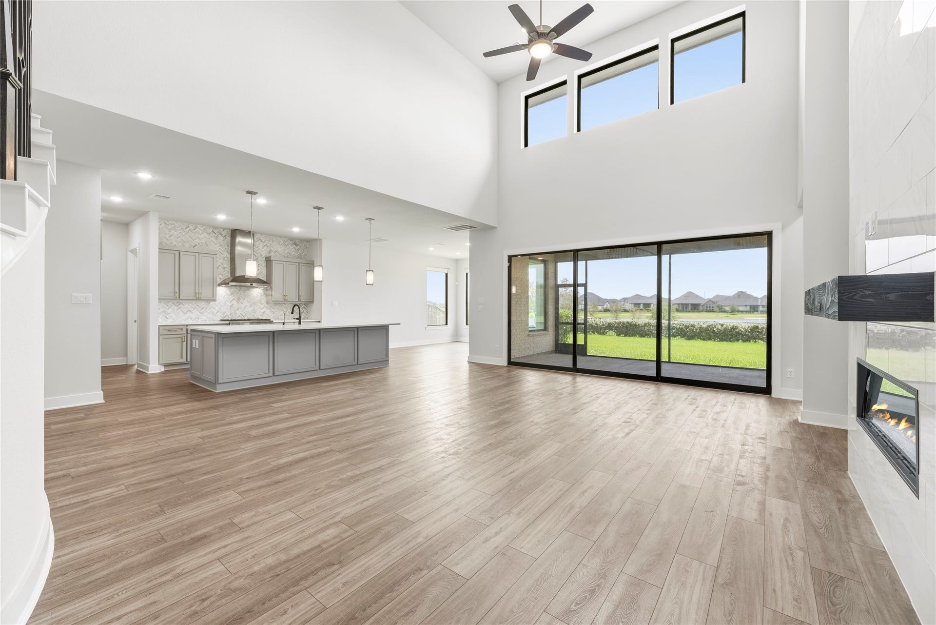 Breathtaking open-concept living area featuring soaring two-story ceilings, wall of glass sliding doors to the patio, modern tile fireplace, and direct flow to the gourmet kitchen.