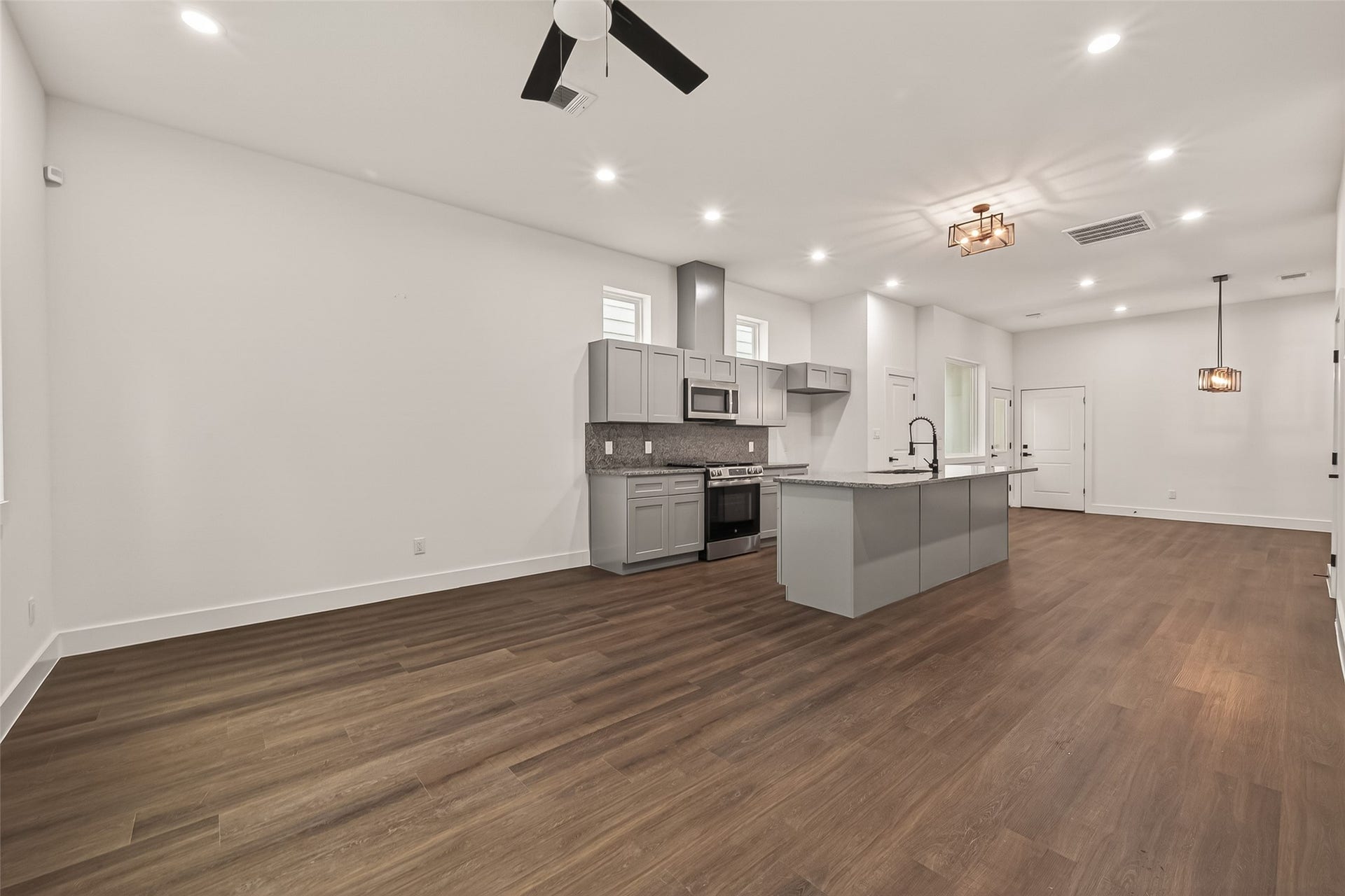 6808 Madrid Street, Houston, TX 77021 This photo showcases a spacious, open-concept living area with a modern kitchen featuring grey cabinets, stainless steel appliances, and a large island. The room has wood flooring, recessed lighting, and stylish ceiling fixtures, providing a clean and contemporary look.
