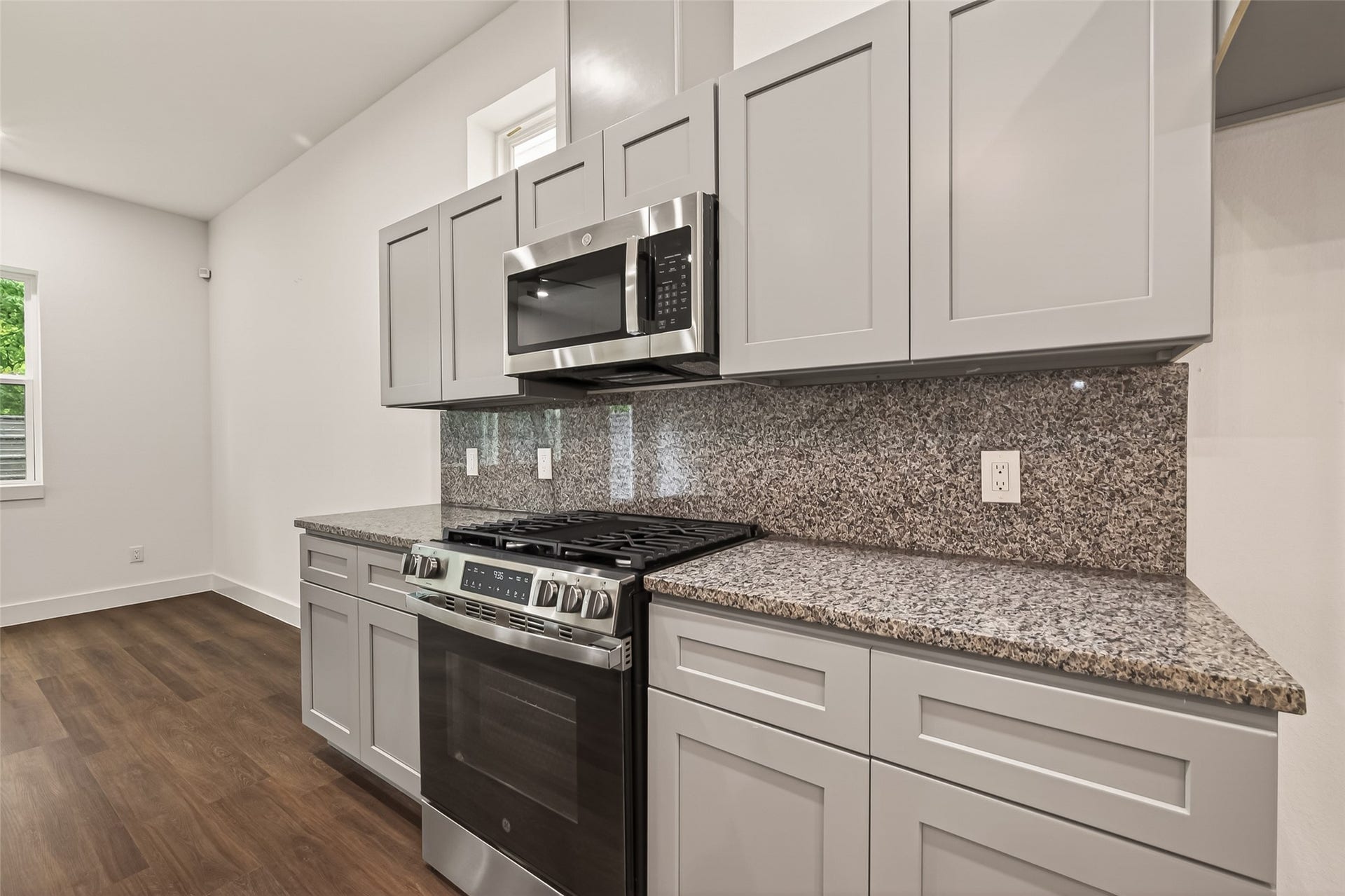 6808 Madrid Street, Houston, TX 77021 Modern kitchen with sleek gray cabinets, stainless steel appliances, and a granite countertop. The room features a gas stove and microwave, with ample storage and a warm wood floor.