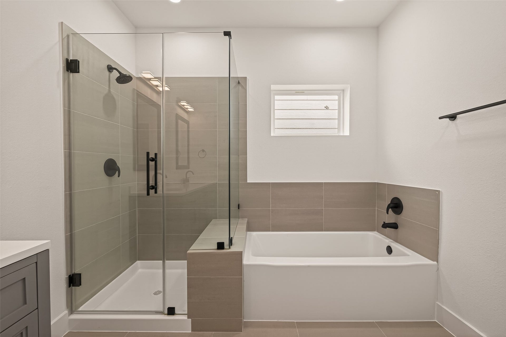 6808 Madrid Street, Houston, TX 77021 This modern bathroom features a sleek glass-enclosed shower and a separate bathtub, both with matte black fixtures. The neutral tiles and bright lighting create a clean, contemporary look.