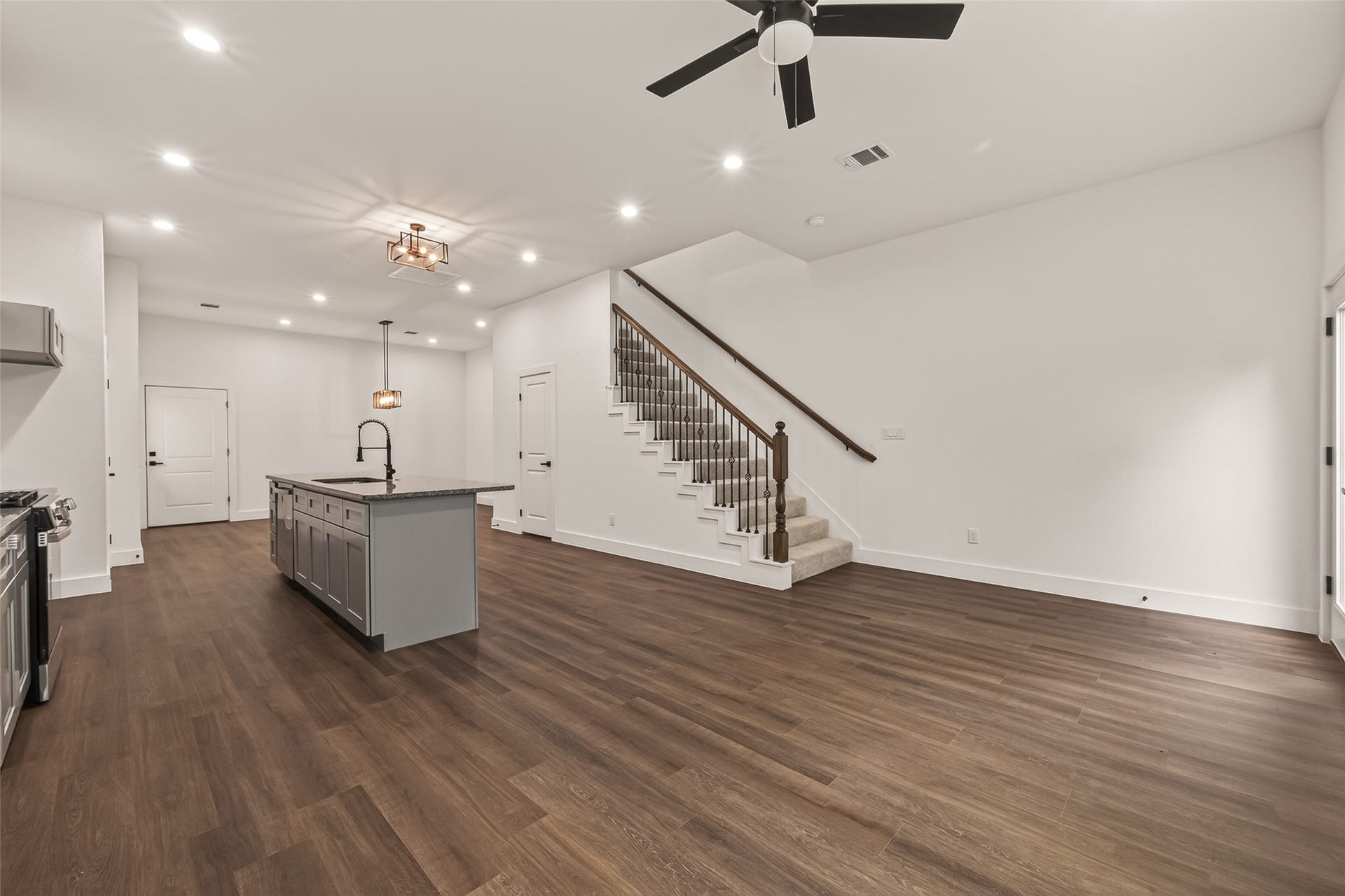 6808 Madrid Street, Houston, TX 77021 This spacious open-concept living area features sleek engineer woodfloors, a modern kitchen island with a dark countertop, and a stylish ceiling fan. The area is well-lit with recessed lighting, and a staircase with wooden railings leads to the upper level, making it ideal for entertaining and comfortable living.