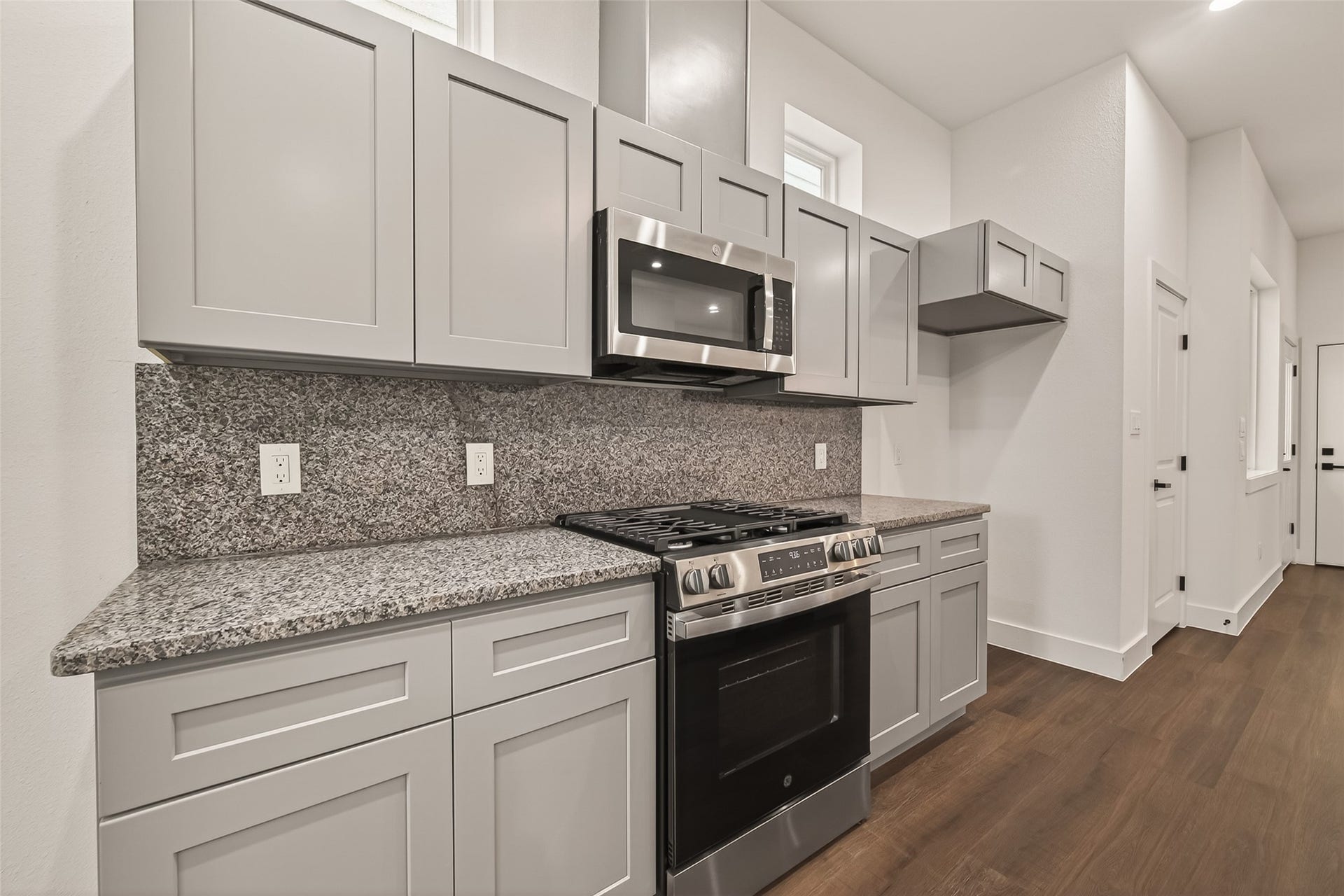 6808 Madrid Street, Houston, TX 77021 This kitchen features modern gray cabinetry, granite countertops, and stainless steel appliances, including a built-in microwave and gas range. The space is well-lit with natural light and has a sleek, contemporary design.