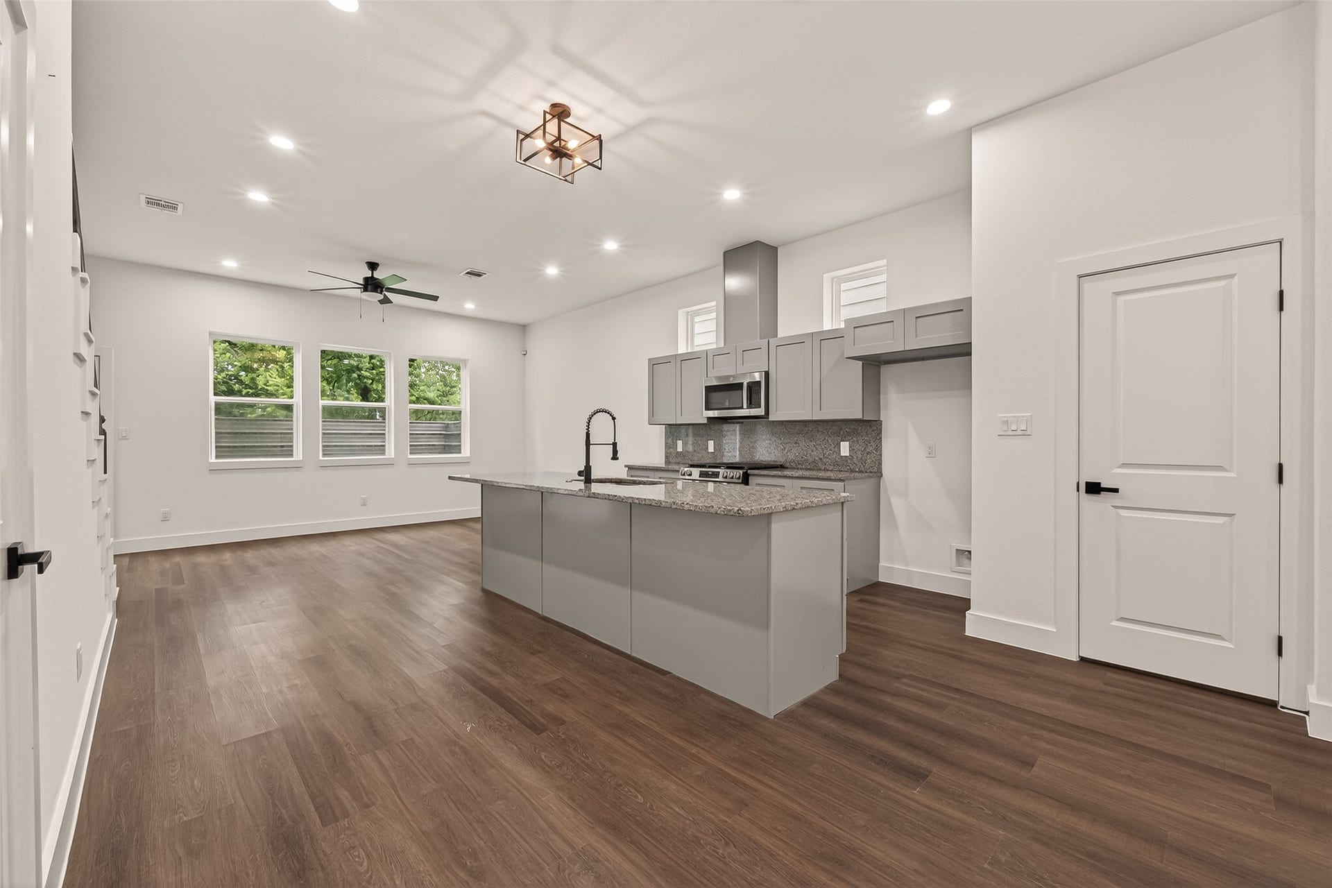 6808 Madrid Street, Houston, TX 77021 This photo showcases a modern, open-concept kitchen and living area with sleek engineer wood floors, neutral walls, and ample natural light from multiple windows. The kitchen features a large island with granite countertops, stainless steel appliances, and stylish gray cabinetry, perfect for entertaining and everyday living.