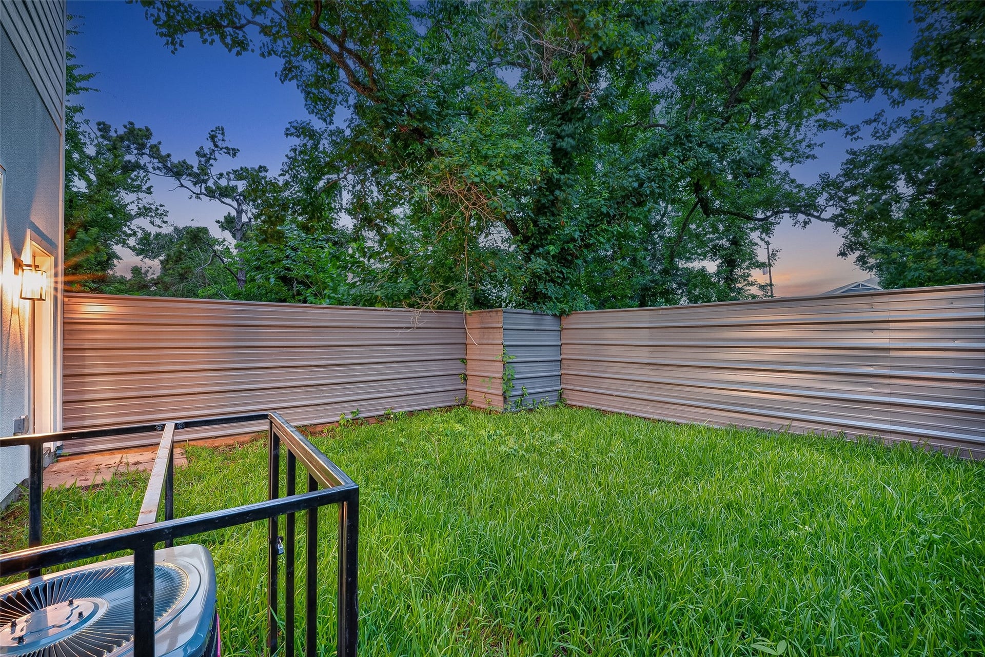 6808 Madrid Street, Houston, TX 77021 This photo shows a small, fenced backyard with lush grass and surrounded by trees, offering privacy and a tranquil atmosphere. A central air conditioning unit is visible, indicating modern amenities.