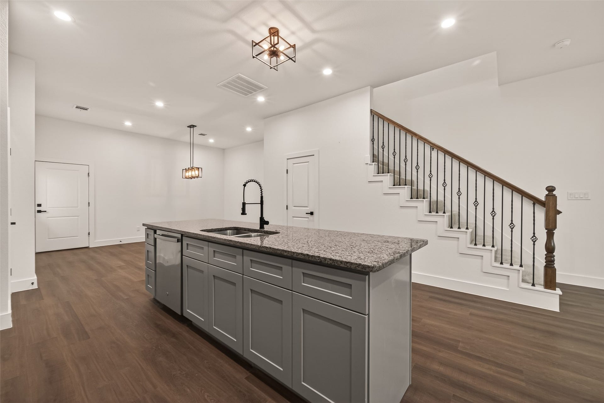 6808 Madrid Street, Houston, TX 77021 This modern home features an open-concept kitchen with a large island, granite countertops, and sleek cabinetry. It has a stylish staircase with decorative iron railing, recessed lighting, and wood flooring, providing a warm and inviting atmosphere.