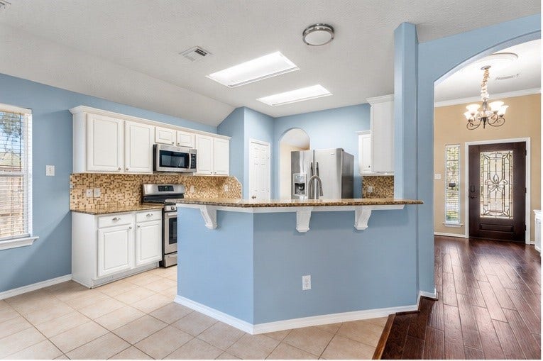 12902 Cascadia Knoll Court, Humble, TX 77346 Kitchen overview featuring white cabinetry, granite countertops, mosaic tile backsplash, stainless steel appliances, and a raised breakfast bar.