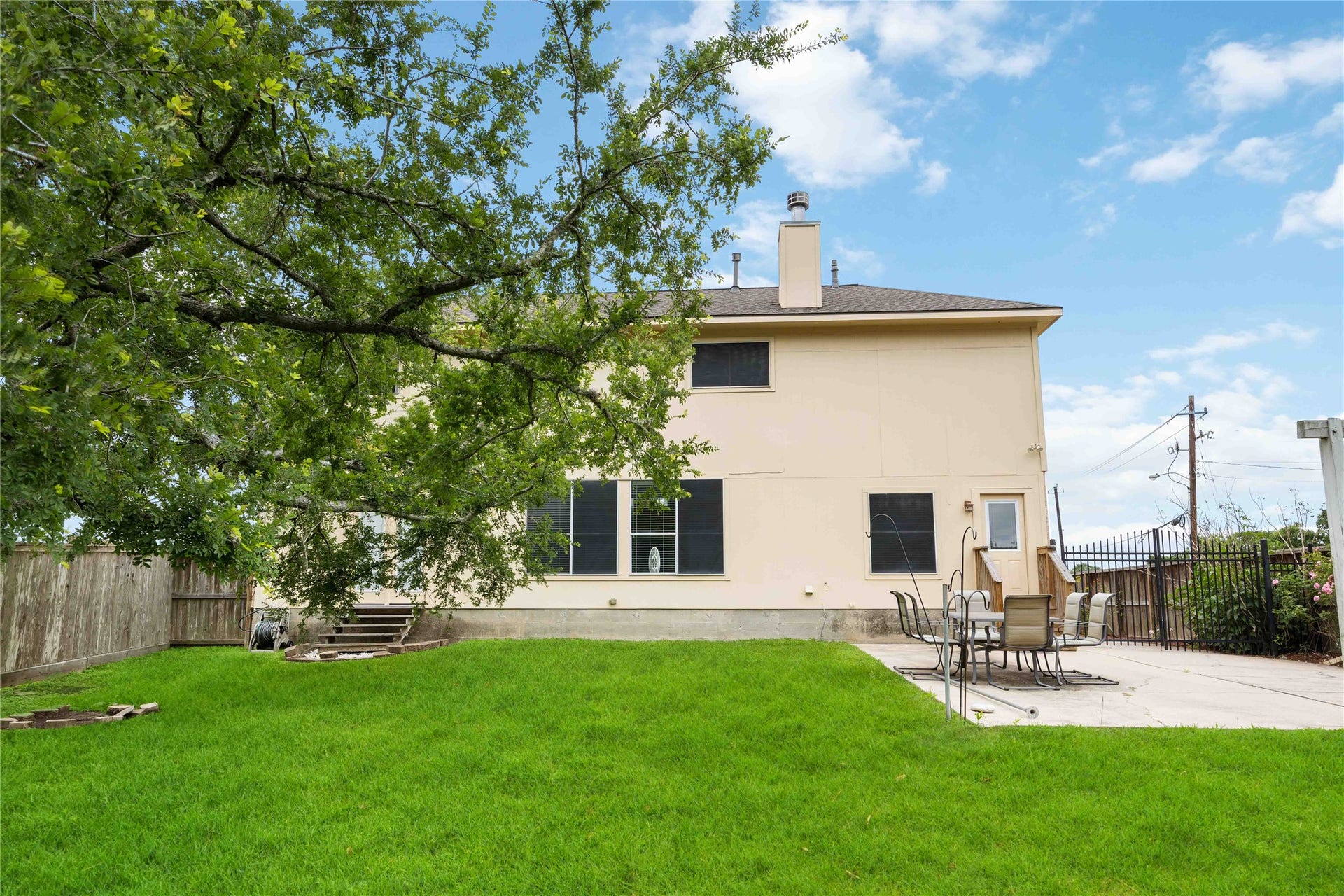 5498 Appleblossom Lane, Friendswood, TX 77546 The backyard of a two-story home with a large green lawn, a spacious patio area with outdoor furniture, and a mature tree providing shade. The space is ideal for relaxation and entertaining.