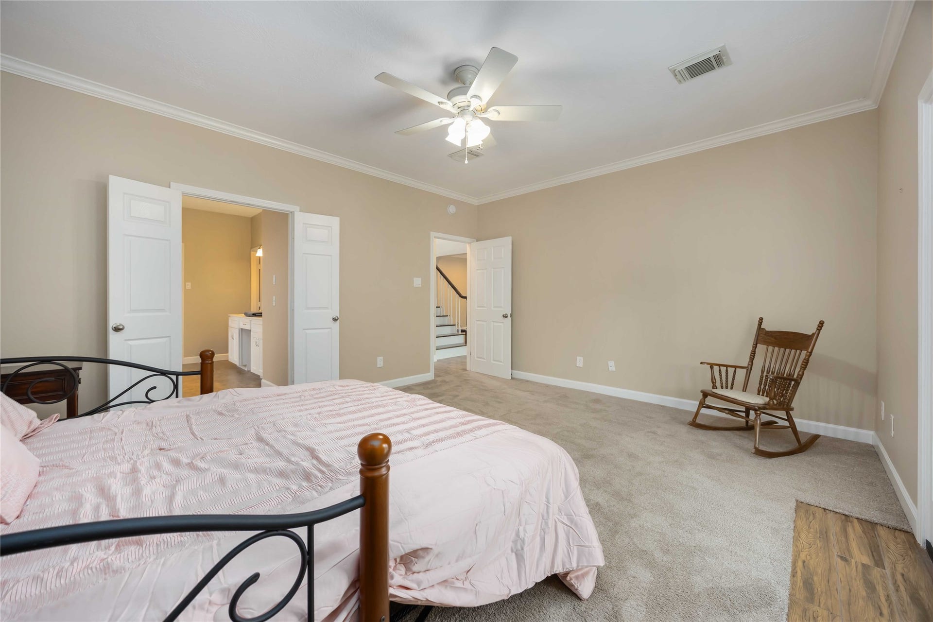 5498 Appleblossom Lane, Friendswood, TX 77546 This spacious primary bedroom features neutral walls, carpet flooring, and a ceiling fan. It includes an ensuite bathroom with double doors and a cozy seating area with a rocking chair.