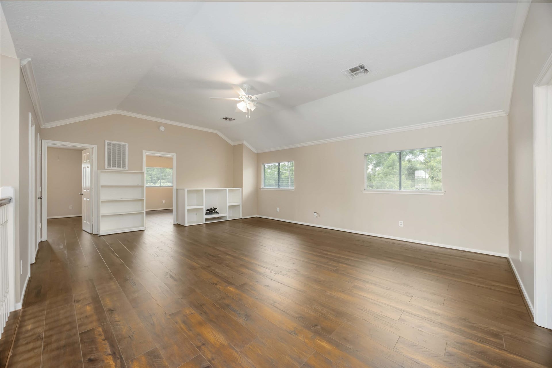 5498 Appleblossom Lane, Friendswood, TX 77546 Spacious room with hardwood floors, neutral walls, and a sloped ceiling. Features built-in shelving and large windows offering natural light, ideal for a versatile living area.