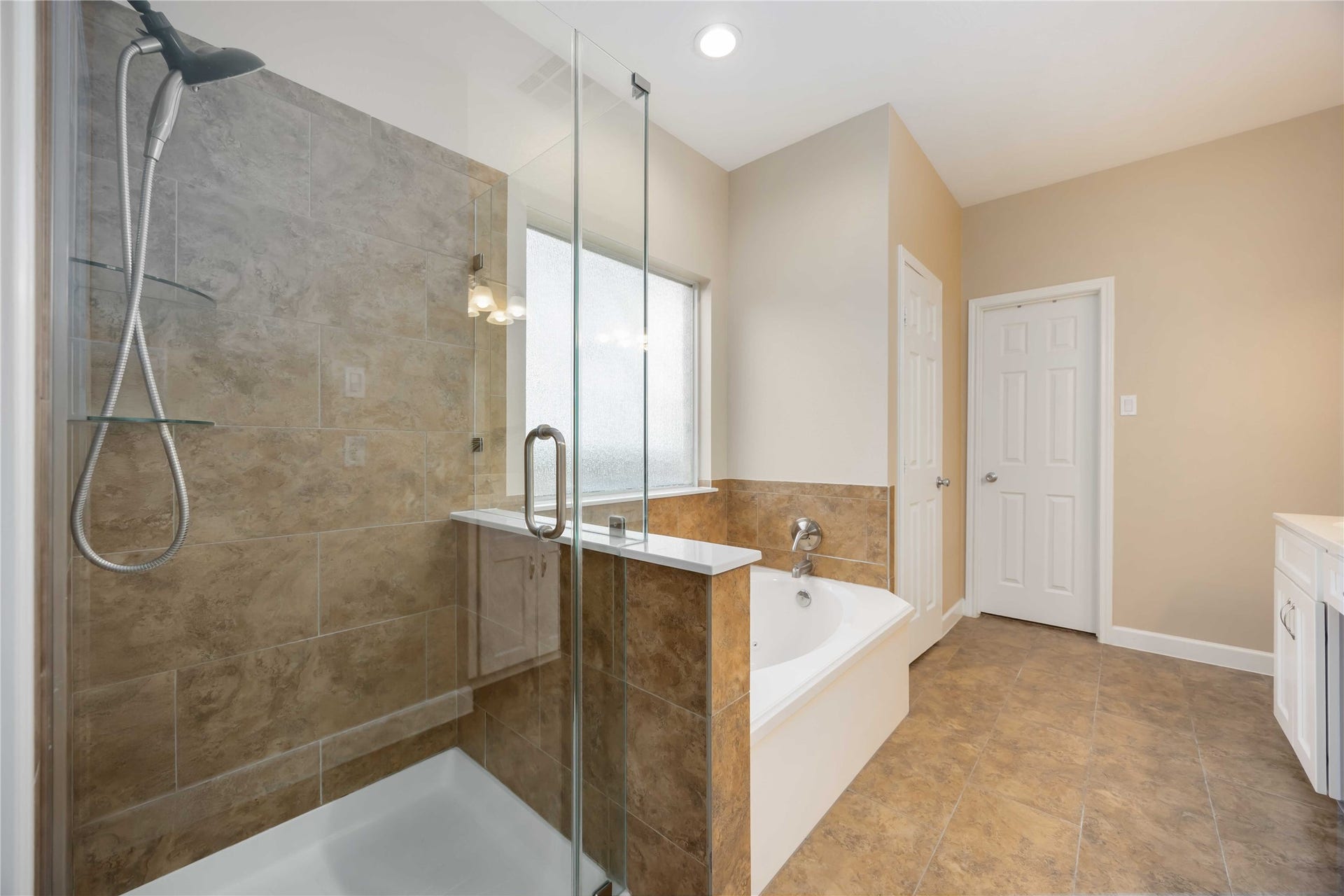 5498 Appleblossom Lane, Friendswood, TX 77546 Modern bathroom with a glass-enclosed shower and a separate bathtub. It features neutral tile flooring and walls, a frosted window for privacy, and ample lighting.