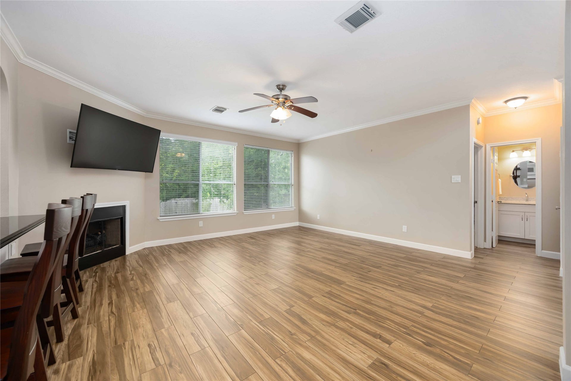 5498 Appleblossom Lane, Friendswood, TX 77546 This spacious living room features wood-style flooring and a cozy fireplace. Large windows offer plenty of natural light, and there's a ceiling fan for added comfort. It connects to a kitchen area with bar seating and has access to a bright bathroom.