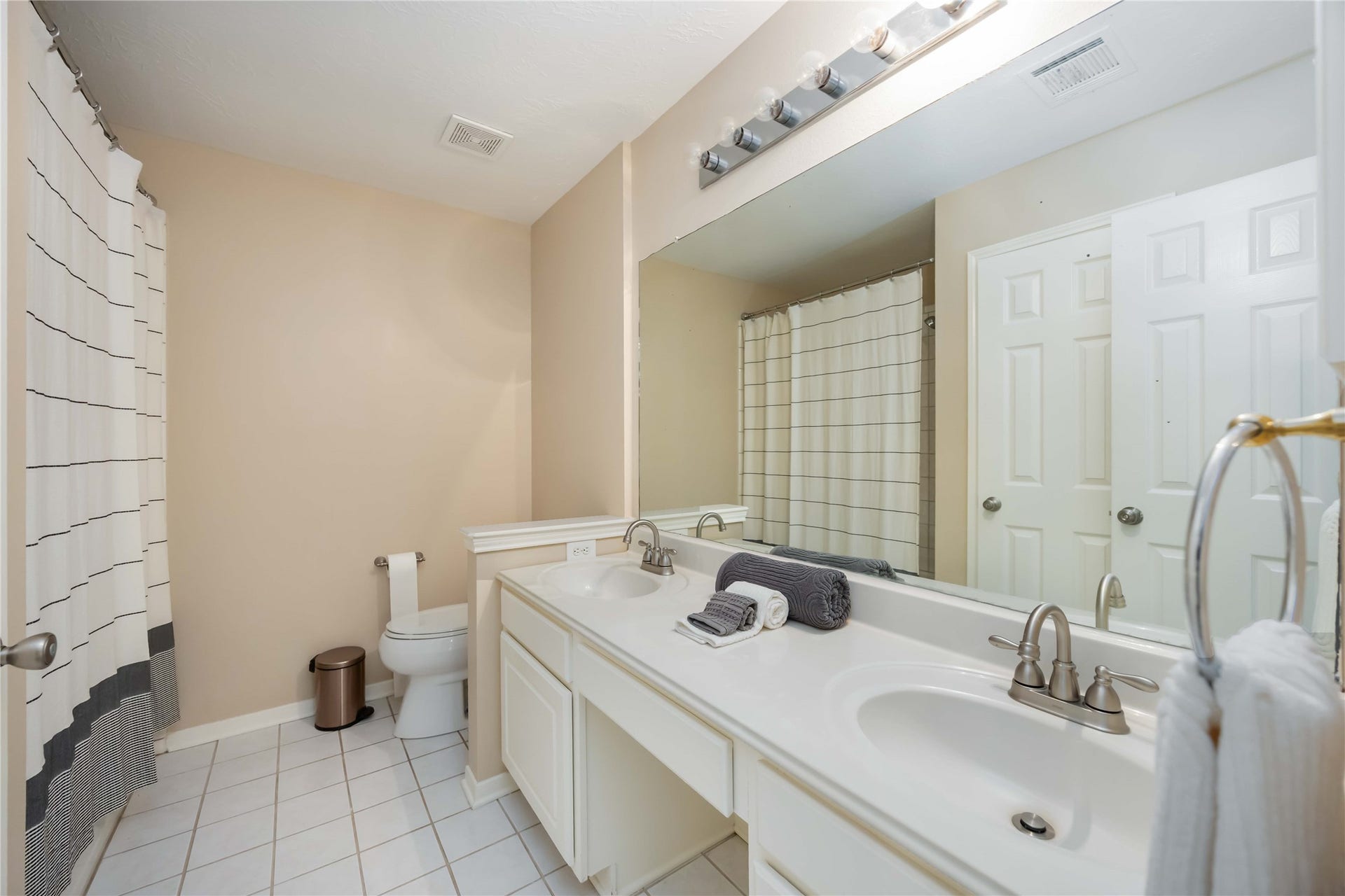 5498 Appleblossom Lane, Friendswood, TX 77546 This bathroom features a double vanity with a large mirror, a shower-tub combo with a striped curtain, neutral walls, and tiled flooring for a clean, modern look.