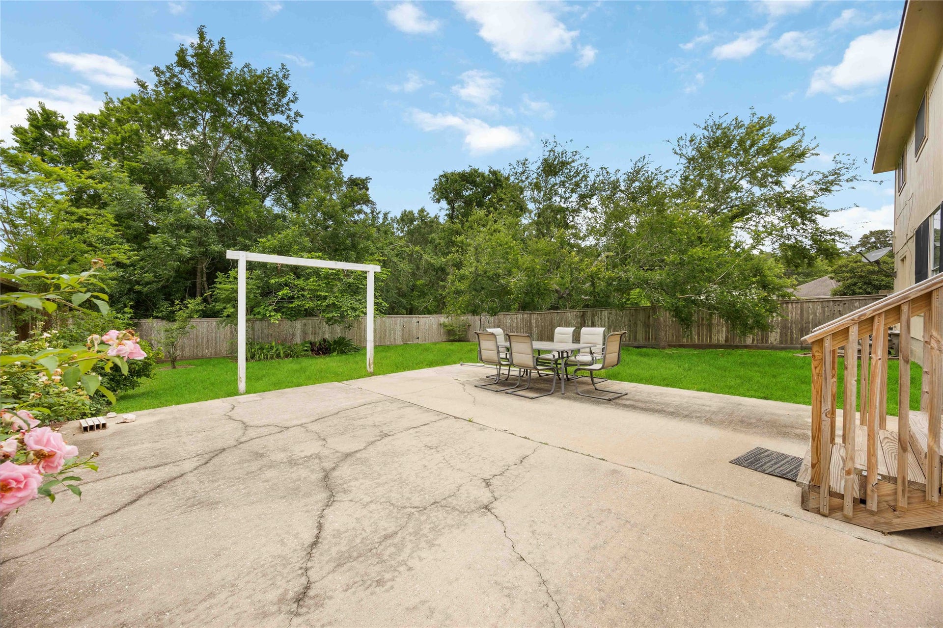 5498 Appleblossom Lane, Friendswood, TX 77546 Spacious backyard with a large concrete patio, perfect for outdoor dining and entertaining. The area features a lush lawn, mature trees for privacy, and a wooden fence. Ideal for family gatherings and relaxation.