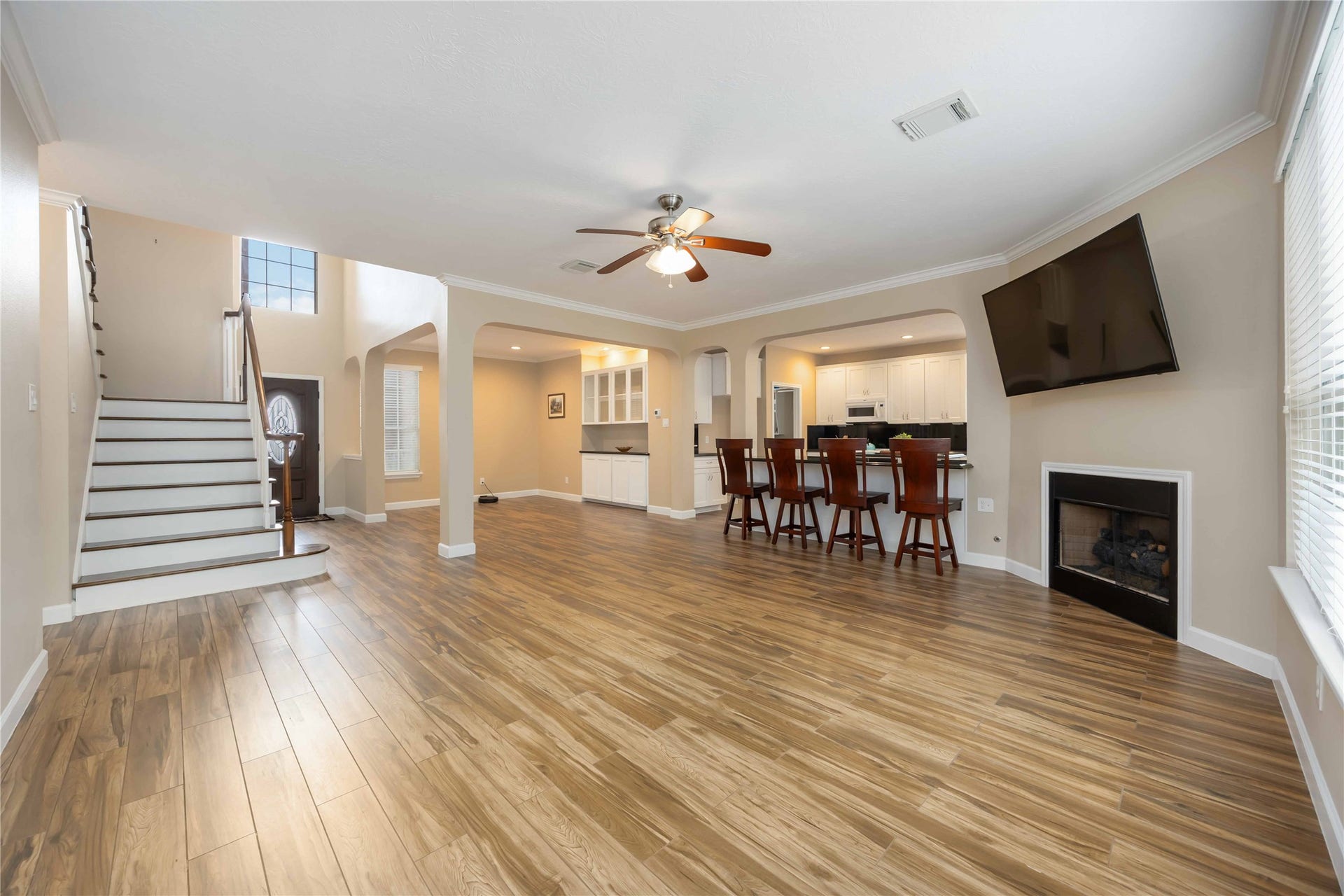 5498 Appleblossom Lane, Friendswood, TX 77546 A spacious, open-concept living area with warm wood flooring, a modern kitchen with bar seating, a cozy fireplace, and a wall-mounted TV. Large windows allow plenty of natural light, and a staircase leads to the upper floor.