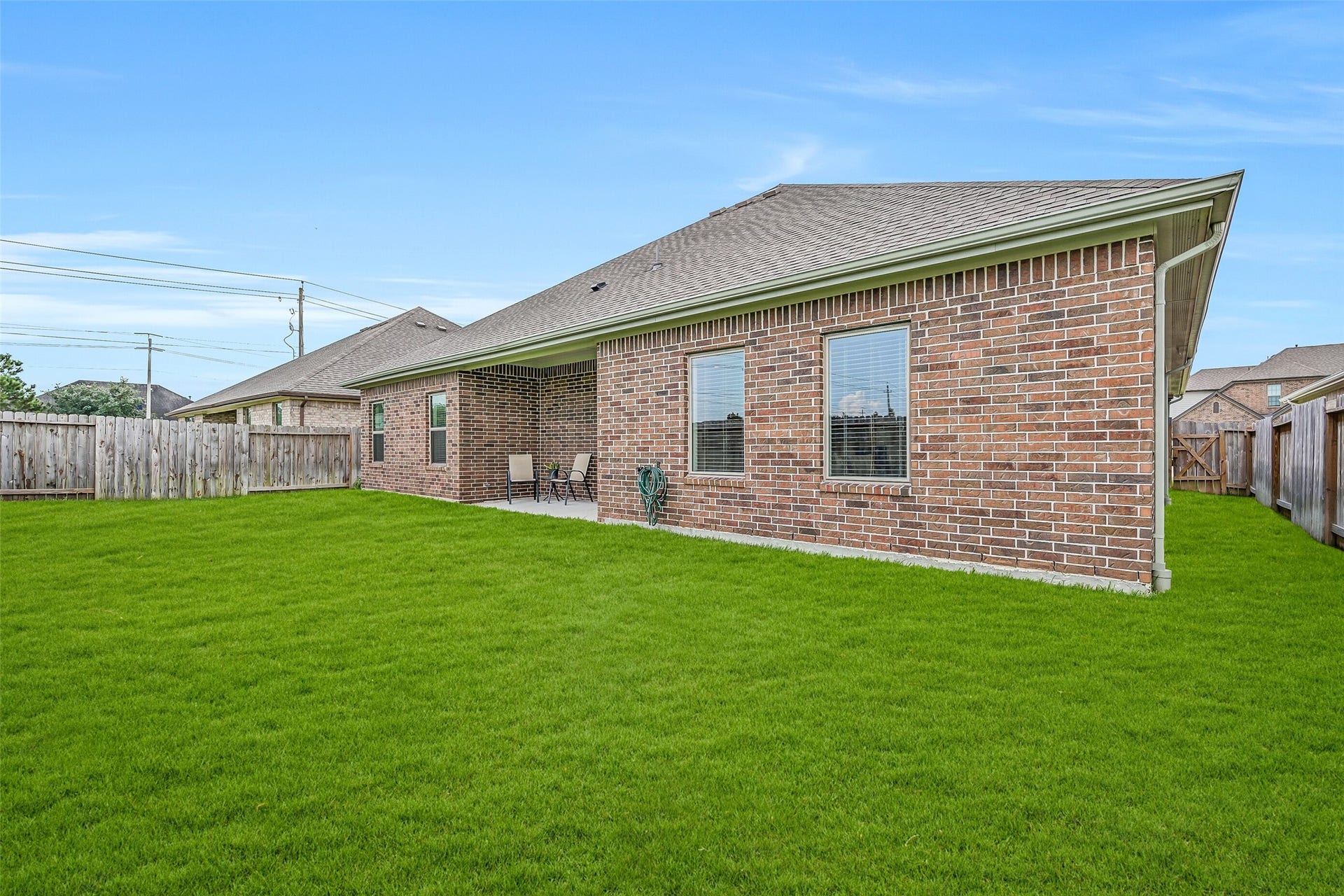 6204 Red Oak Court, League City, TX 77573 A final view showcases the home's brick rear exterior, covered patio and expansive lawn, with multiple rear-facing windows connecting the light-filled interior living spaces to the backyard.