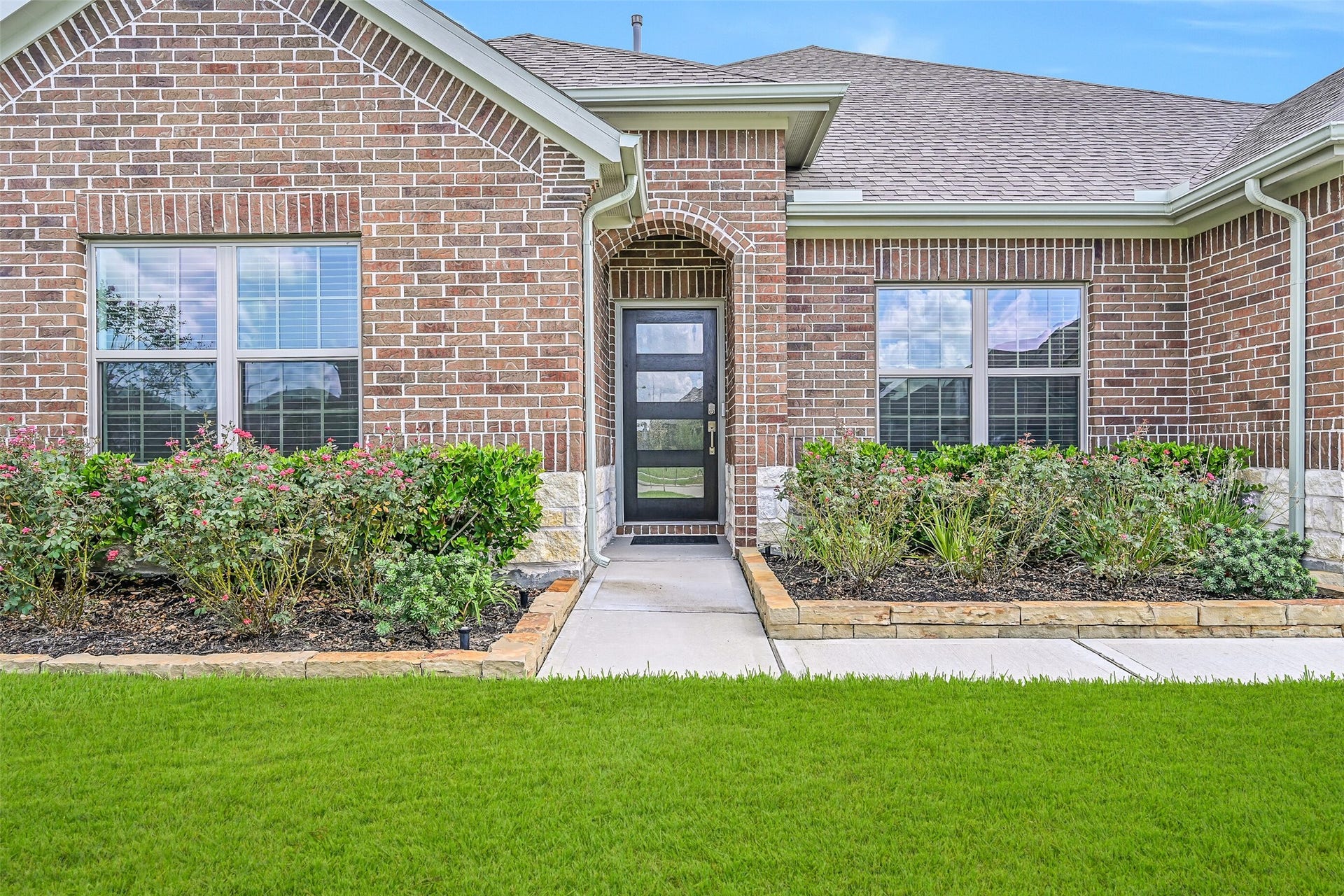 6204 Red Oak Court, League City, TX 77573 A closer look at the inviting front elevation showcases colorful established landscaping, brick & Austin limestone details and a recessed arched entry with a southwest facing contemporary style glass-panel front door.