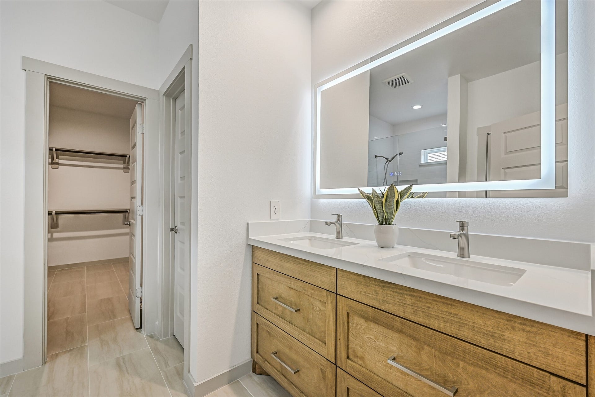 6204 Red Oak Court, League City, TX 77573 The primary bath features a long dual-sink vanity with warm wood-tone cabinetry, sleek fixtures and an impressive illuminated mirror, while an adjoining walk-in closet keeps storage conveniently close at hand.