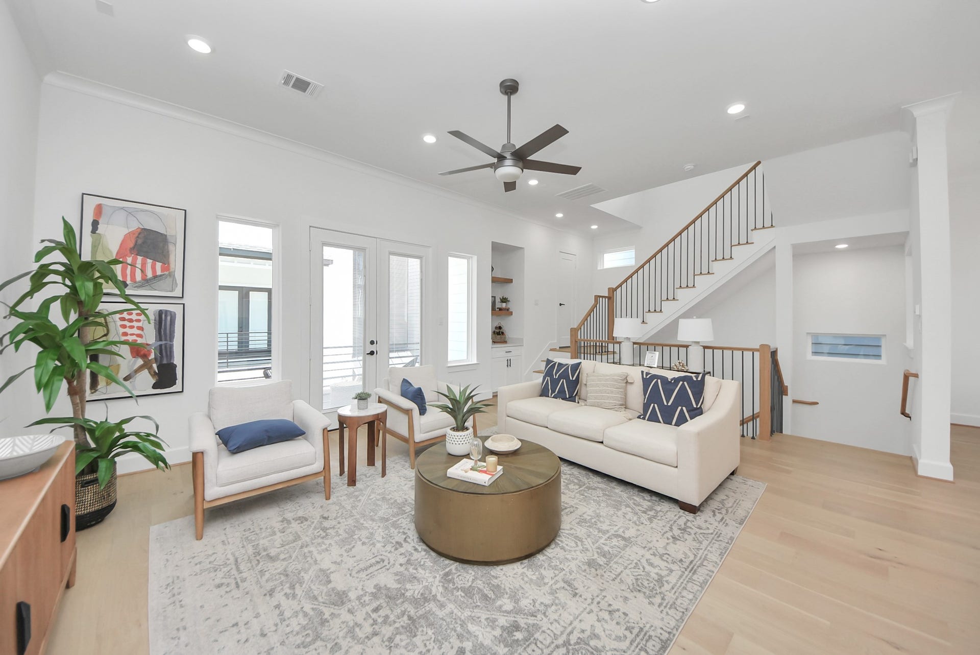 923 Fisher Street, #E, Houston, TX 77018 This modern, open-concept living area combines style and comfort effortlessly. Light wood floors and abundant natural light create an airy atmosphere, while a sleek kitchen with white cabinetry and gold pendant lighting adds a touch of elegance. The adjoining living space, featuring contemporary furnishings and a ceiling fan, offers a perfect setting for both entertaining and relaxing.