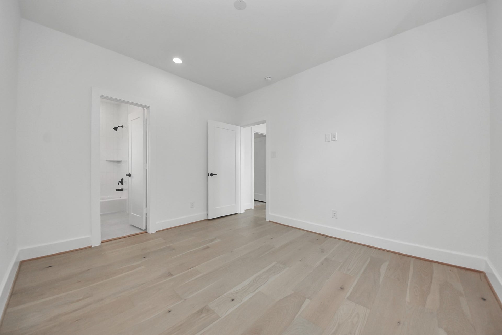 923 Fisher Street, #E, Houston, TX 77018 A clean, bright room with light wood flooring, white walls, and recessed lighting features two doors, one leading to a bathroom. The spaces modern, neutral design provides a versatile layout ready for personal touches.