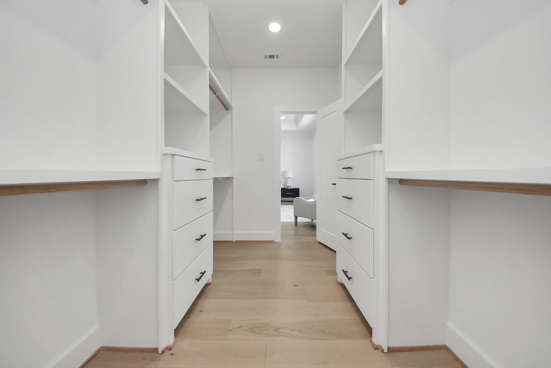 923 Fisher Street, #E, Houston, TX 77018 Step into this expansive walk-in closet, featuring ample shelving, drawers, and hanging space. Light wood flooring and white cabinetry create a bright, modern environment, offering plenty of storage and organization for everyday living.