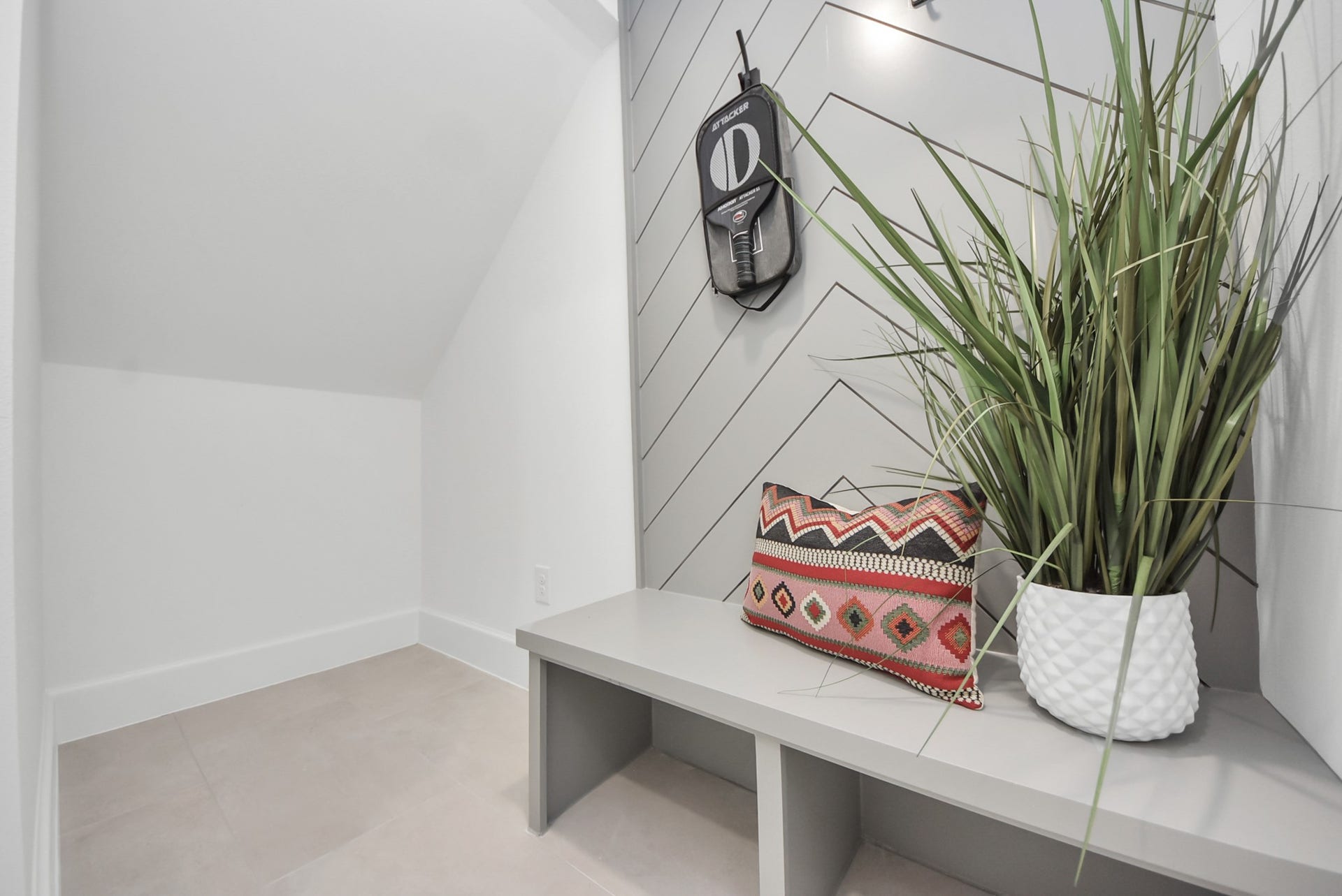 923 Fisher Street, #E, Houston, TX 77018 This cozy nook invites you to relax beneath a sloped ceiling, highlighted by a modern chevron accent wall. A built-in bench with a decorative pillow and plant creates a charming spot ideal for a reading corner or a small, functional storage area.