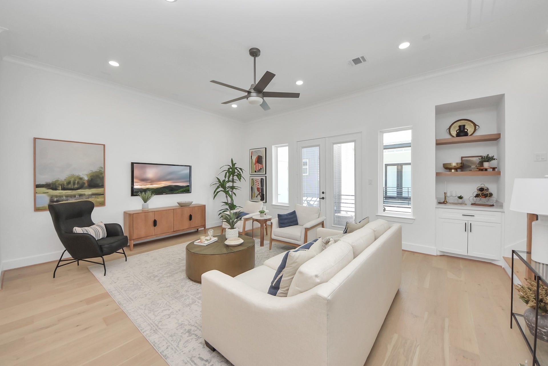 923 Fisher Street, #E, Houston, TX 77018 Step into this bright and airy living room, where modern decor and light wood flooring create an inviting atmosphere. A cozy sofa and armchair complement the sleek ceiling fan, while built-in shelves, large windows, and doors to the outdoor area seamlessly blend functionality with styleperfect for both relaxation and entertaining.