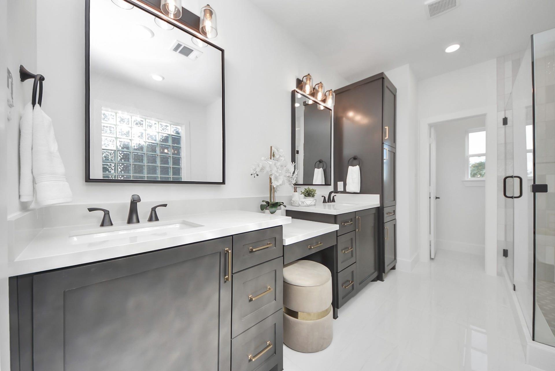 923 Fisher Street, #E, Houston, TX 77018 The modern bathroom impresses with dual vanities in dark cabinetry, white countertops, and stylish black fixtures. Elegant mirrors with overhead lighting, a large glass-enclosed shower, and abundant natural light create a bright, airy, and sophisticated space.