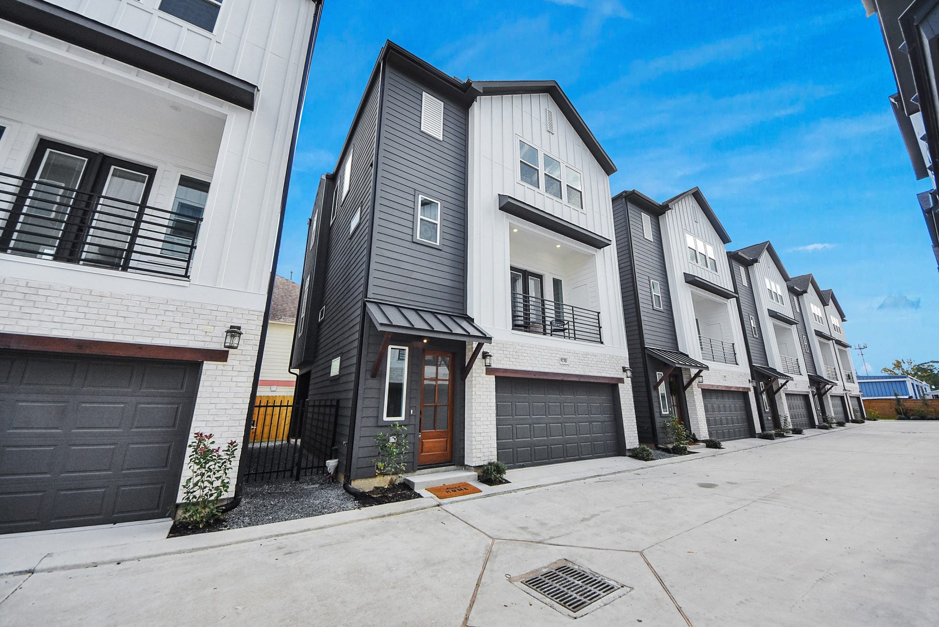 923 Fisher Street, #E, Houston, TX 77018 This modern townhouse welcomes you with a sleek exterior in white and dark gray siding, a warm wooden door, a two-car garage, and a balcony. A small landscaped area enhances curb appeal, making it perfect for contemporary living.