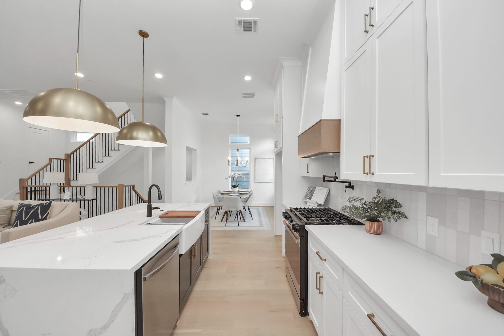 923 Fisher Street, #E, Houston, TX 77018 Experience this modern, open-concept kitchen with sleek white cabinetry, a large marble island, and elegant pendant lighting. The kitchen flows seamlessly into the dining area, with a view of the staircase leading to the upper floor, enhancing the spacious feel.