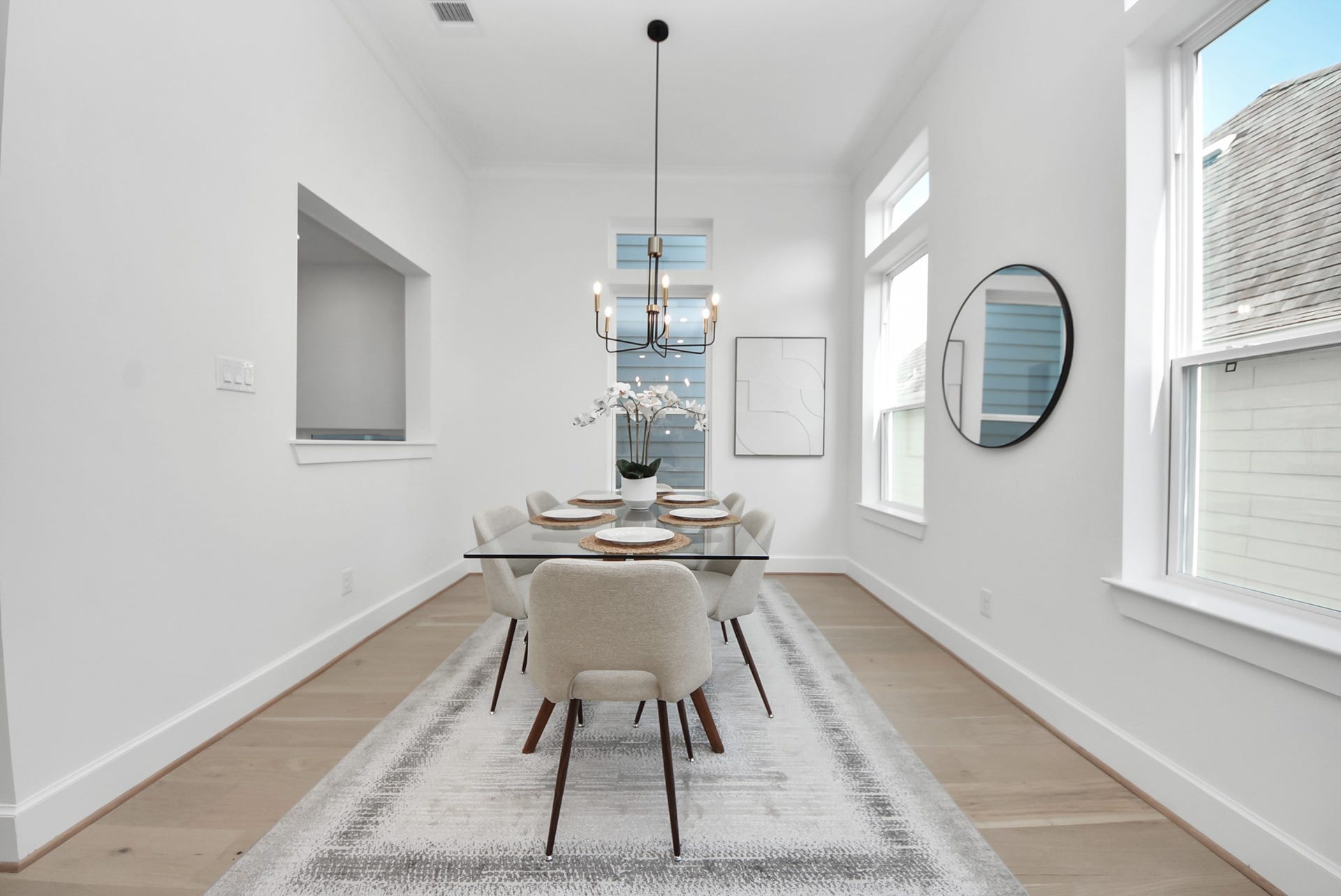923 Fisher Street, #E, Houston, TX 77018 Welcome to this bright, modern dining room, featuring a sleek glass table with seating for six under a contemporary chandelier. Large windows fill the space with natural light, while the neutral color palette and minimalist decor create an inviting atmosphere perfect for meals and gatherings.