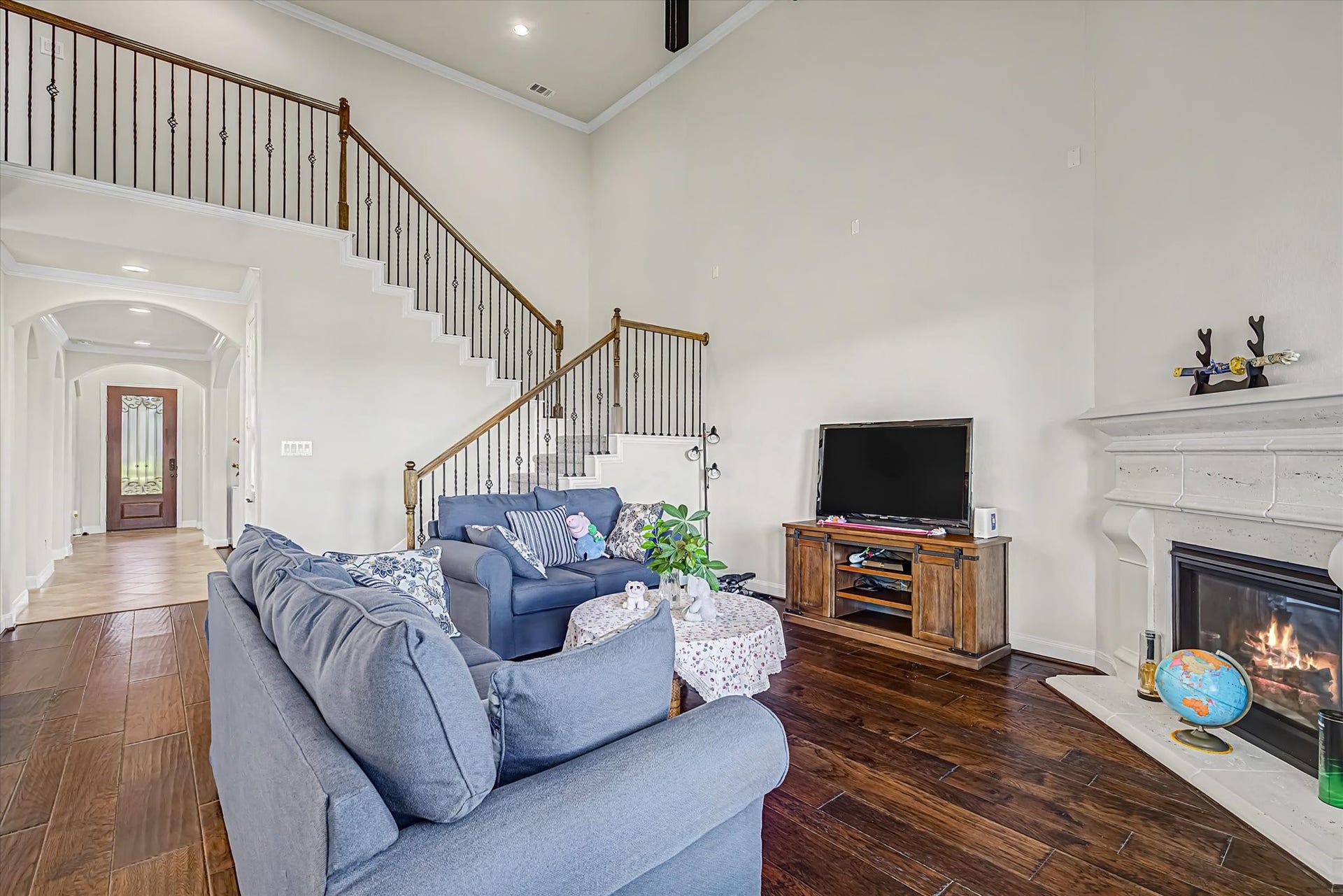 20302 Bandera Lake Lane, Richmond, TX 77407 Elegant living room featuring high ceilings, a grand staircase, and a cozy fireplace, complemented by rich hardwood floors.