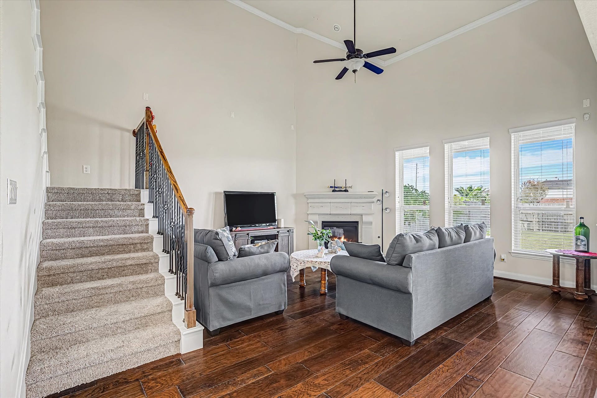 20302 Bandera Lake Lane, Richmond, TX 77407 Spacious living room with high ceilings, featuring a cozy fireplace, large windows for natural light, and elegant hardwood flooring, complemented by a carpeted staircase leading to the upper level.