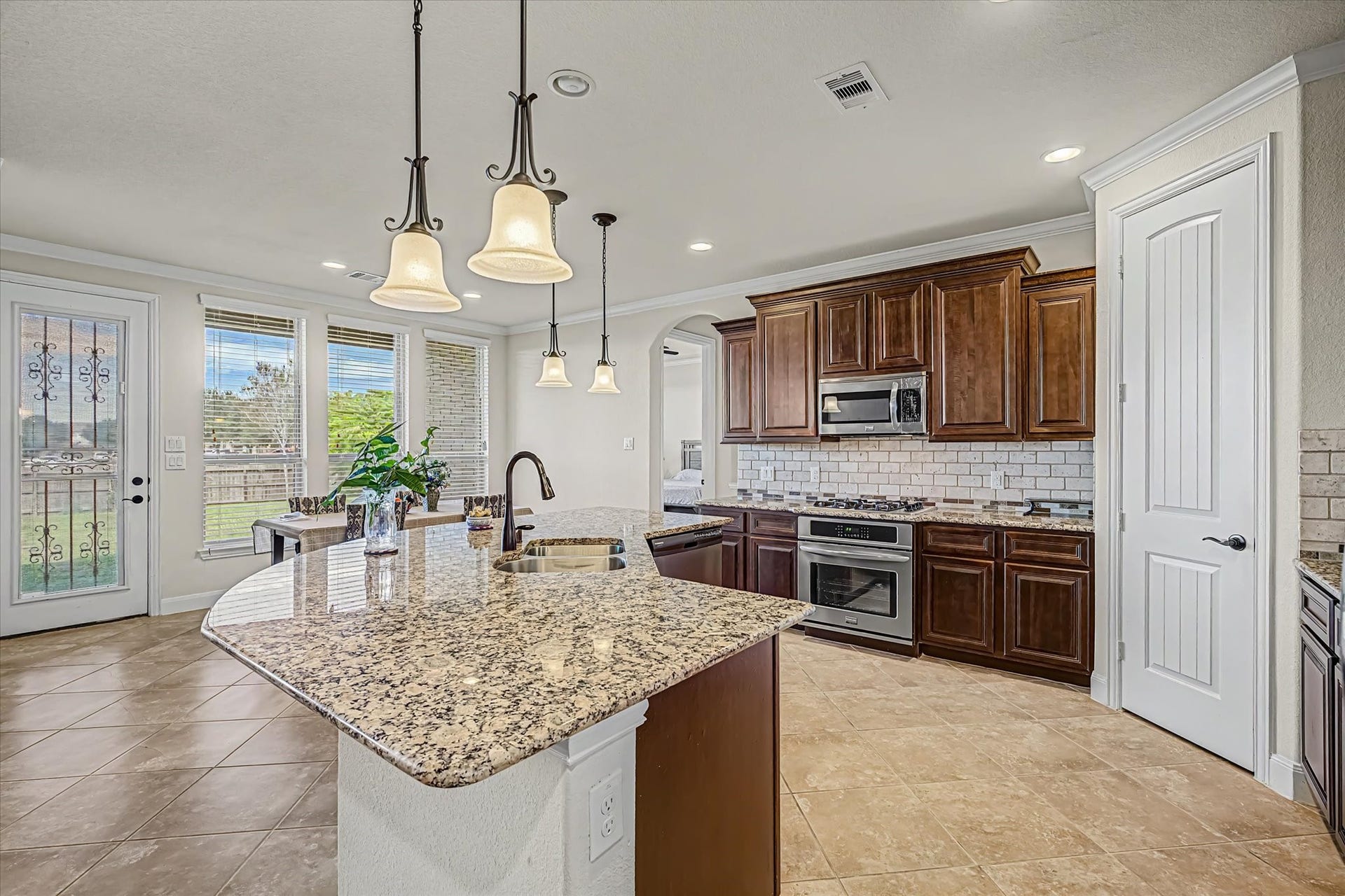 20302 Bandera Lake Lane, Richmond, TX 77407 Elegant kitchen featuring granite countertops, rich wooden cabinetry, and stainless steel appliances, with a spacious island and pendant lighting.