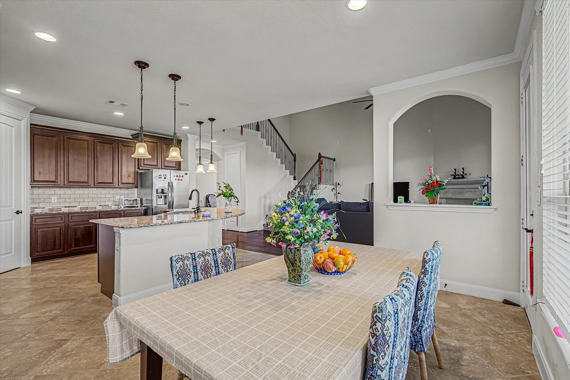 20302 Bandera Lake Lane, Richmond, TX 77407 Spacious open-plan kitchen and breakfast area features elegant wood cabinetry, granite countertops, and stylish pendant lighting, seamlessly connecting to a cozy living space and staircase.
