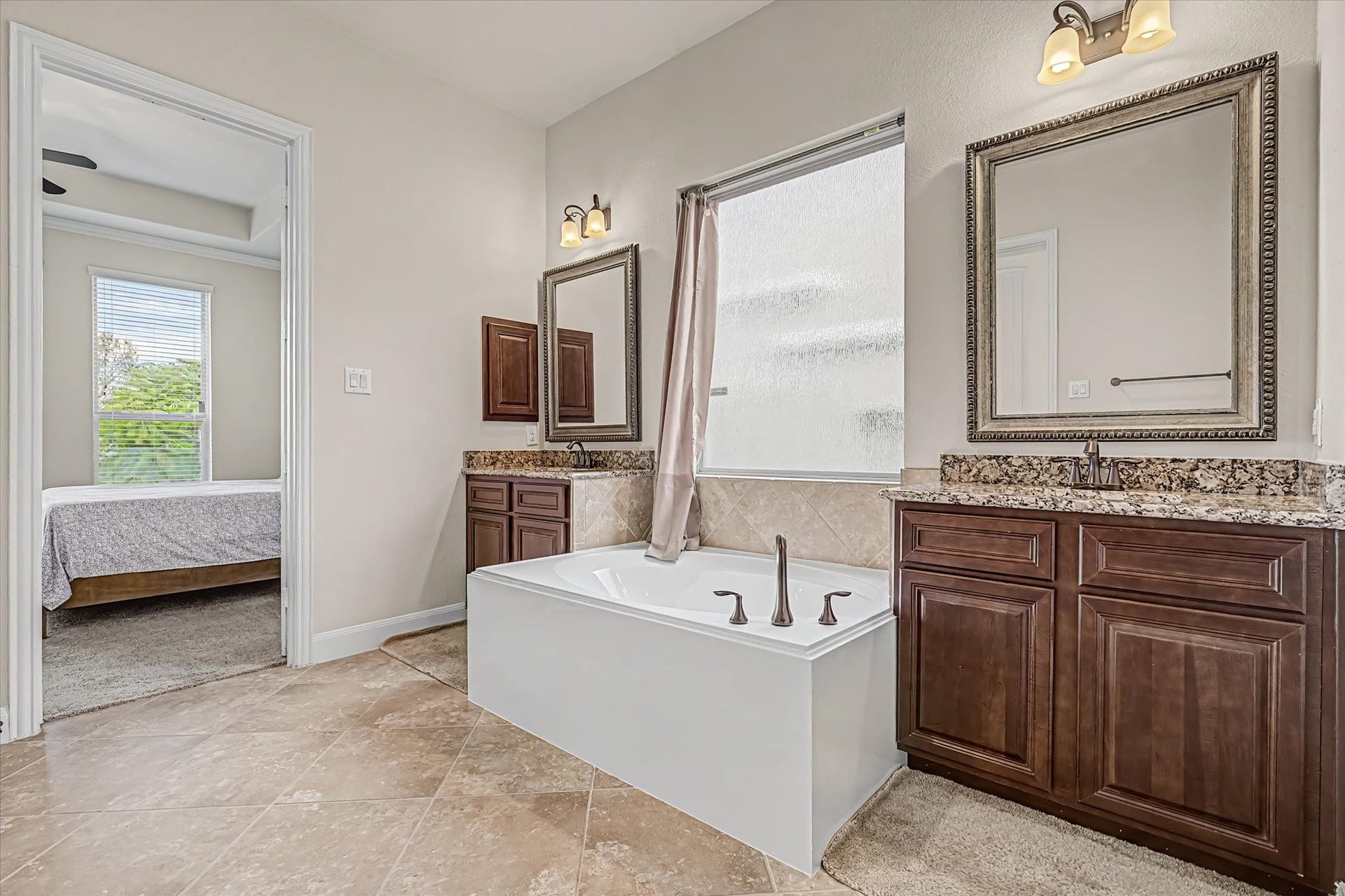 20302 Bandera Lake Lane, Richmond, TX 77407 Elegant bathroom with dual vanities, rich wood cabinetry, and a spacious soaking tub, seamlessly connected to primary bedroom.