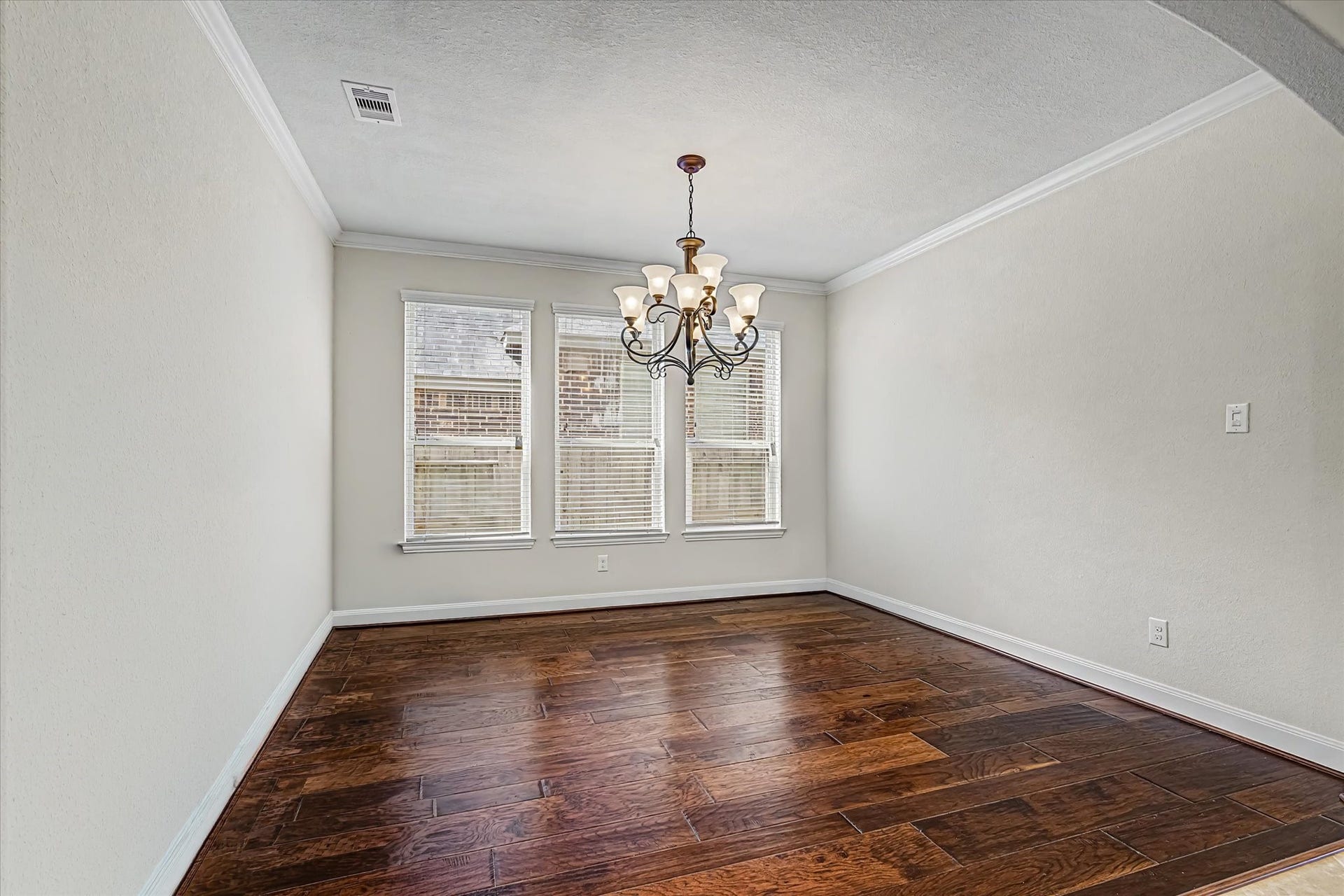 20302 Bandera Lake Lane, Richmond, TX 77407 Elegant dining room with rich hardwood flooring, abundant natural light from three large windows, and a classic chandelier adding a touch of sophistication.