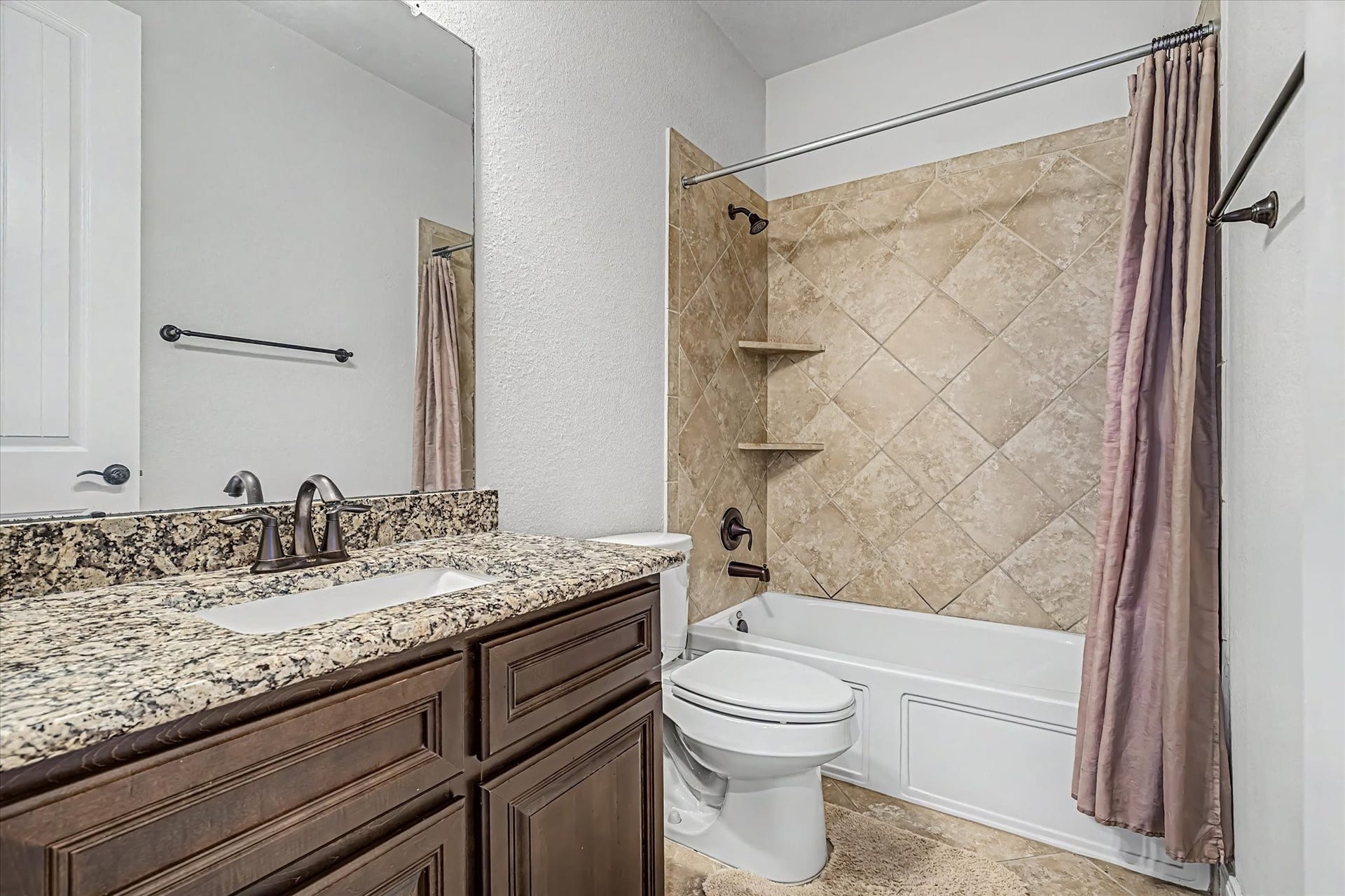 20302 Bandera Lake Lane, Richmond, TX 77407 Elegant secondary bathroom downstairs featuring a granite countertop, rich wood cabinetry, and a stylish tiled shower with built-in shelving.