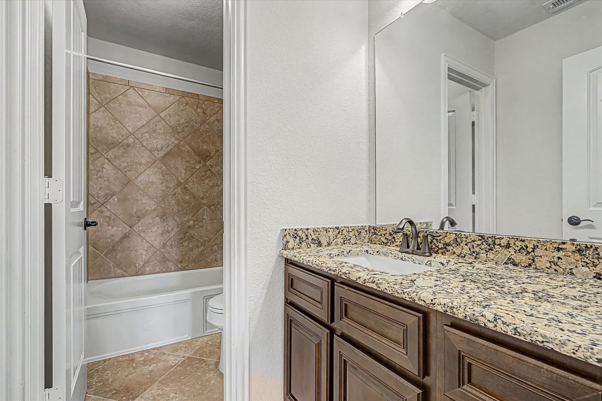 20302 Bandera Lake Lane, Richmond, TX 77407 Elegant bathroom featuring a granite countertop with dual sinks, rich wood cabinetry, and a tub with stylish tile surround.