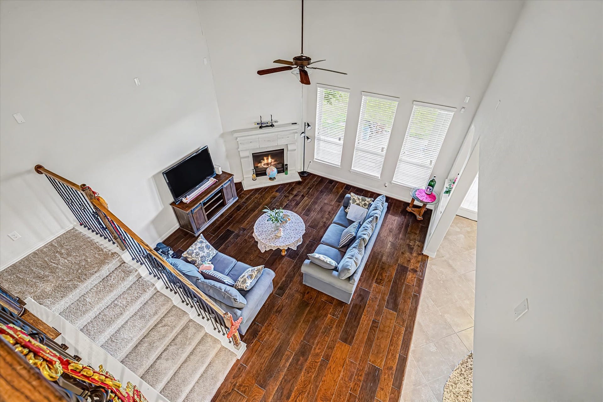 20302 Bandera Lake Lane, Richmond, TX 77407 Spacious living room with rich hardwood floors, a cozy fireplace, and abundant natural light from large windows, viewed from an elegant staircase.