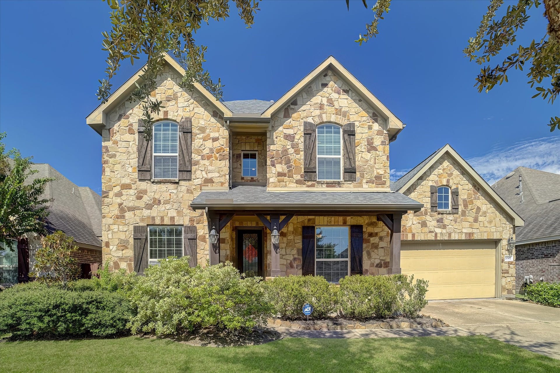 20302 Bandera Lake Lane, Richmond, TX 77407 Charming two-story home with a beautiful stone facade, classic shutters, and a welcoming front porch. The lush landscaping enhances its curb appeal, and the attached garage offers convenience.