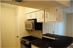 6001 Reims Road, #1202, Houston, TX 77036 Cozy kitchen with white cabinets, black countertops, and a built-in microwave. Compact layout ideal for efficiency.