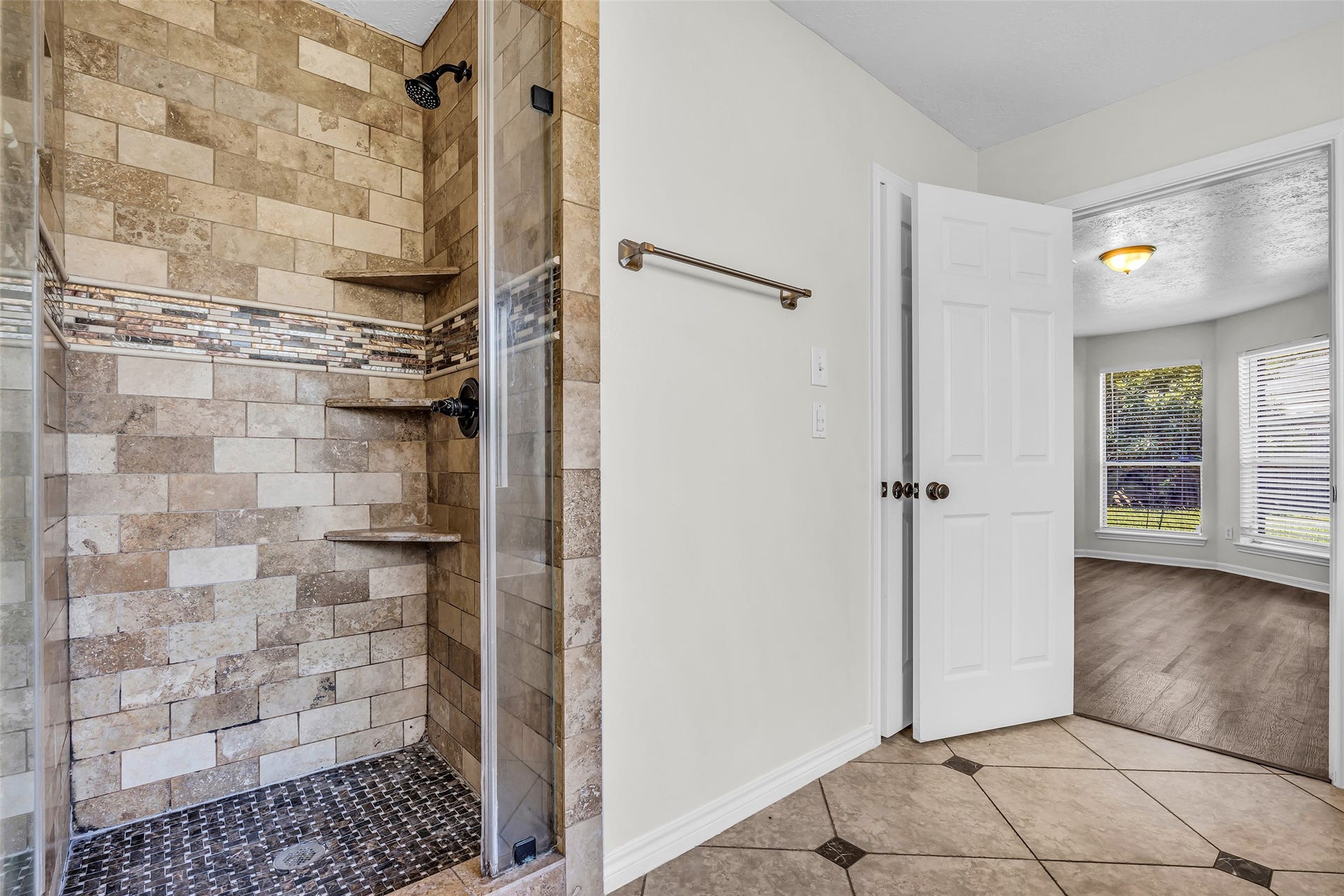 A walk-in shower with stone-look tile, built-in shelves and a glass door.
