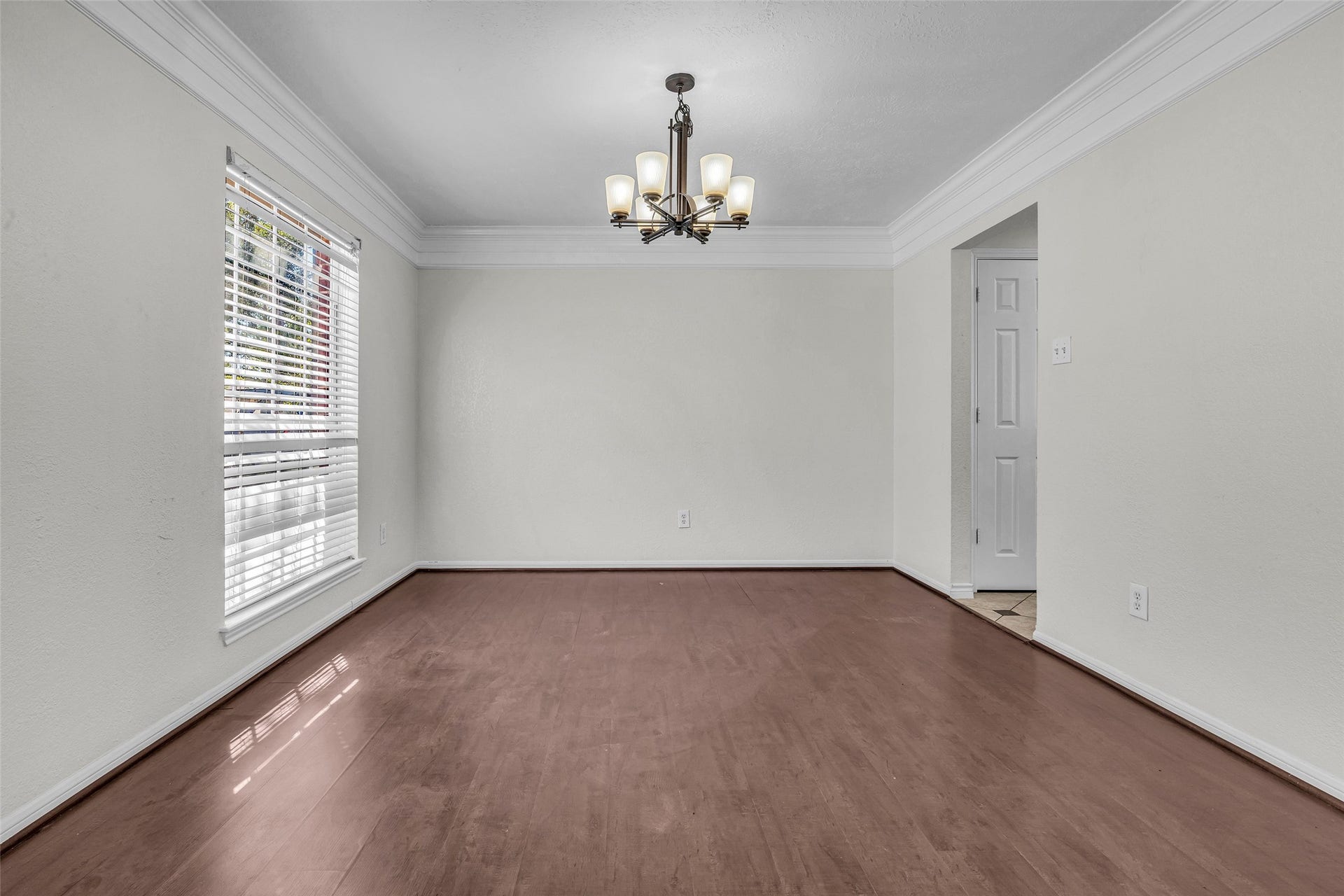 Host holiday dinners in the formal dining room, with crown molding, a chandelier and wood-look flooring.