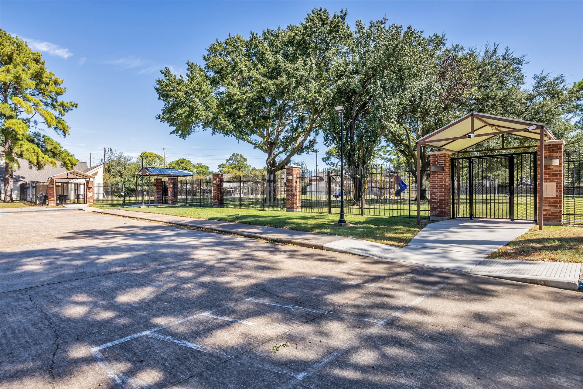 A gated community park entrance with shade trees and sidewalks.
