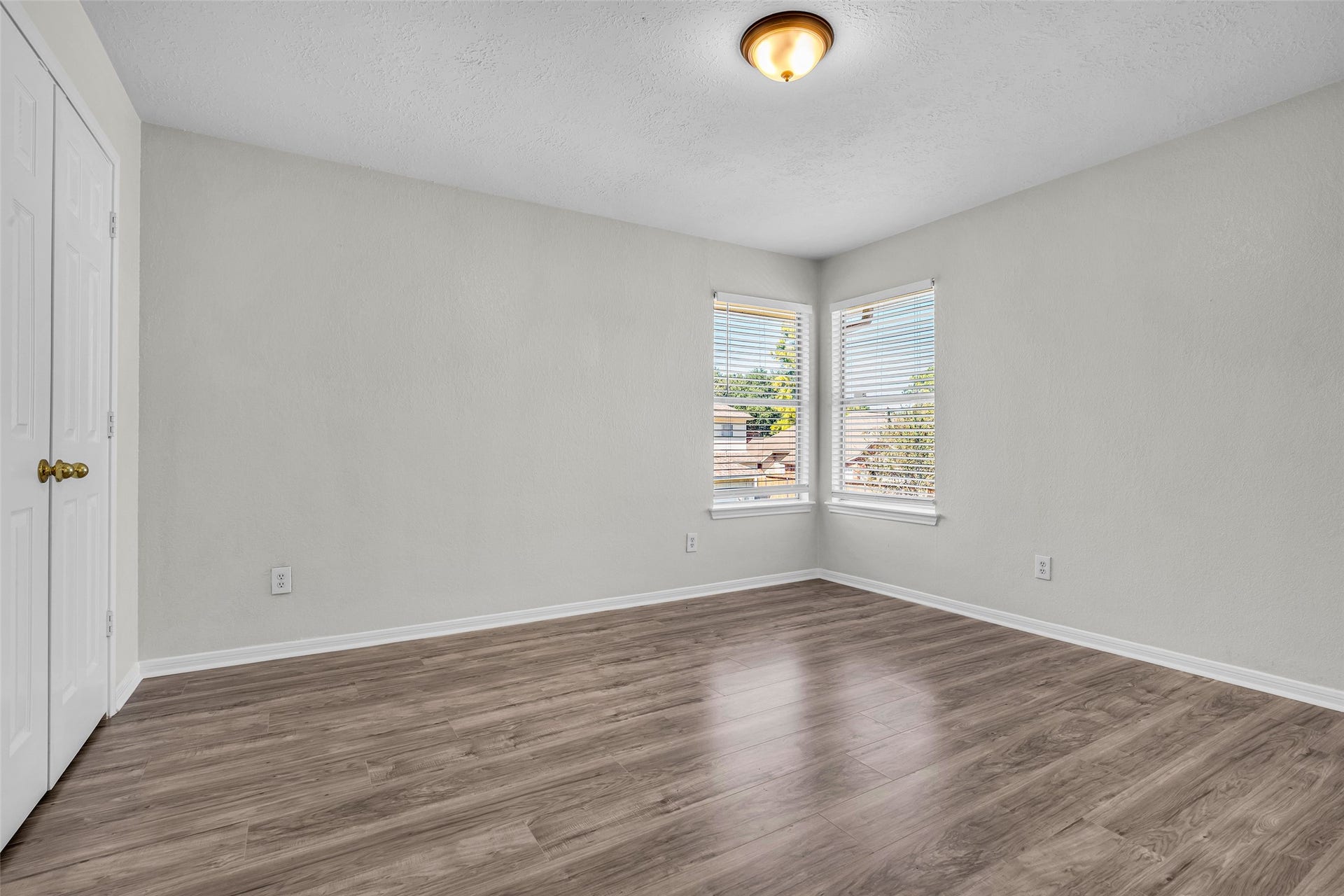 A bright secondary bedroom with two windows and wood-look flooring.