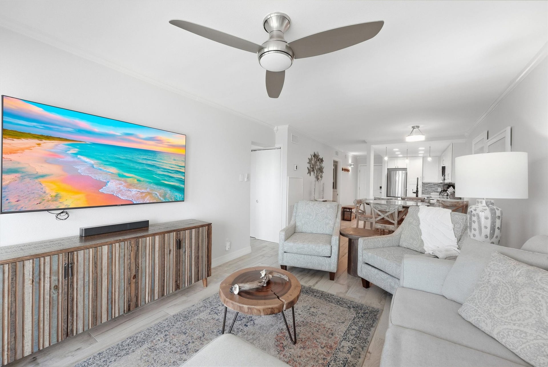 7310 Seawall Boulevard, #1105, Galveston, TX 77551 Bright and inviting living space featuring a stylish ceiling fan, cozy seating, and a vibrant wall-mounted TV. The open layout seamlessly connects to a modern kitchen, perfect for entertaining.