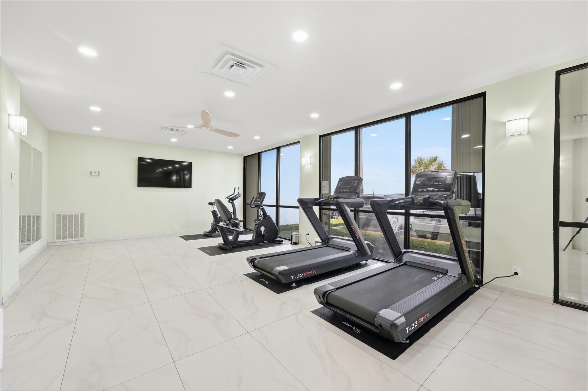 7310 Seawall Boulevard, #1105, Galveston, TX 77551 Modern fitness center with large windows, featuring treadmills, exercise bikes, and a wall-mounted TV for an enjoyable workout experience.