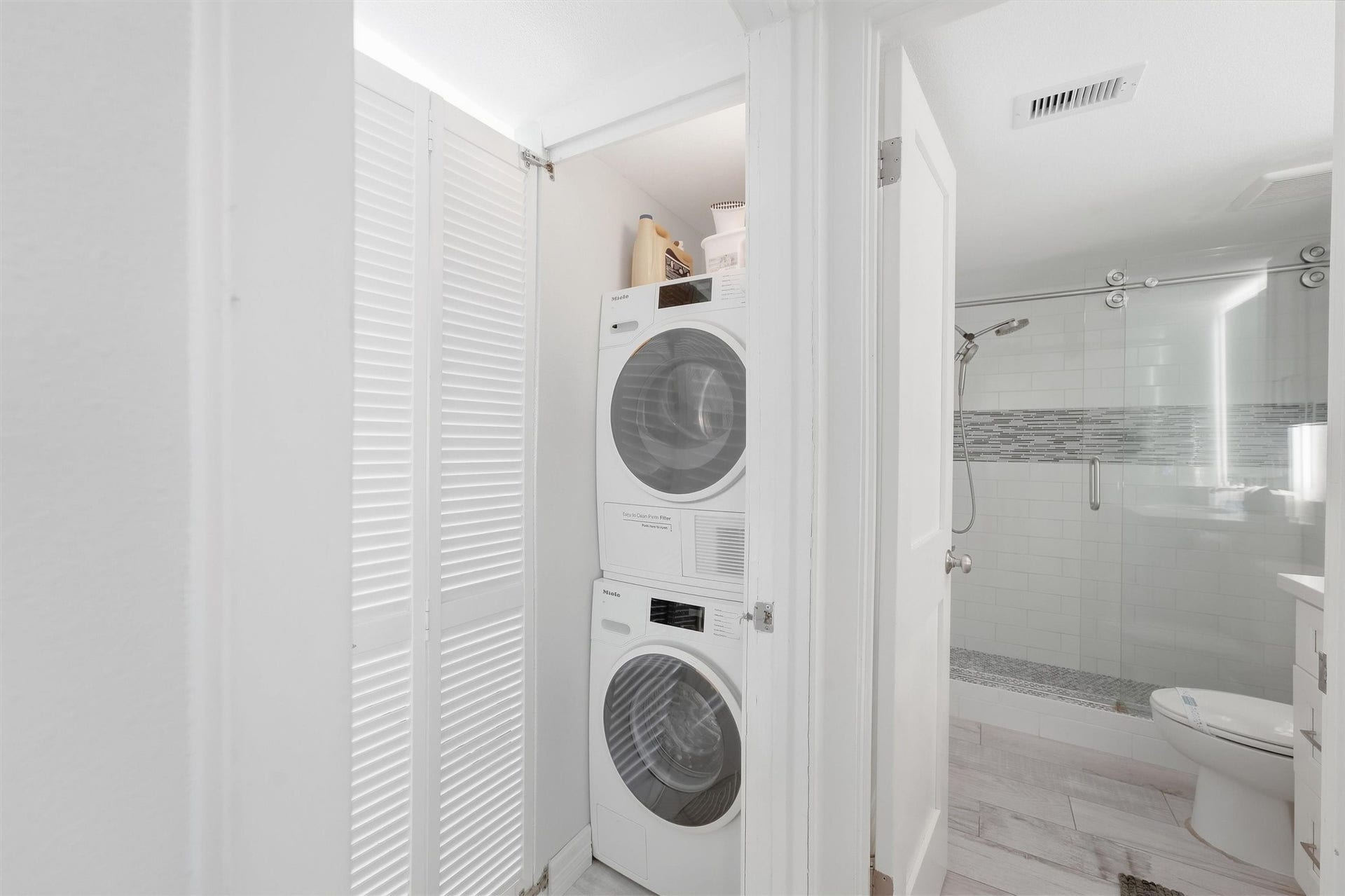7310 Seawall Boulevard, #1105, Galveston, TX 77551 Convenient in-unit laundry with a sleek stacked washer and dryer set, adjacent to a modern bathroom featuring a glass-enclosed shower and updated tilework.
