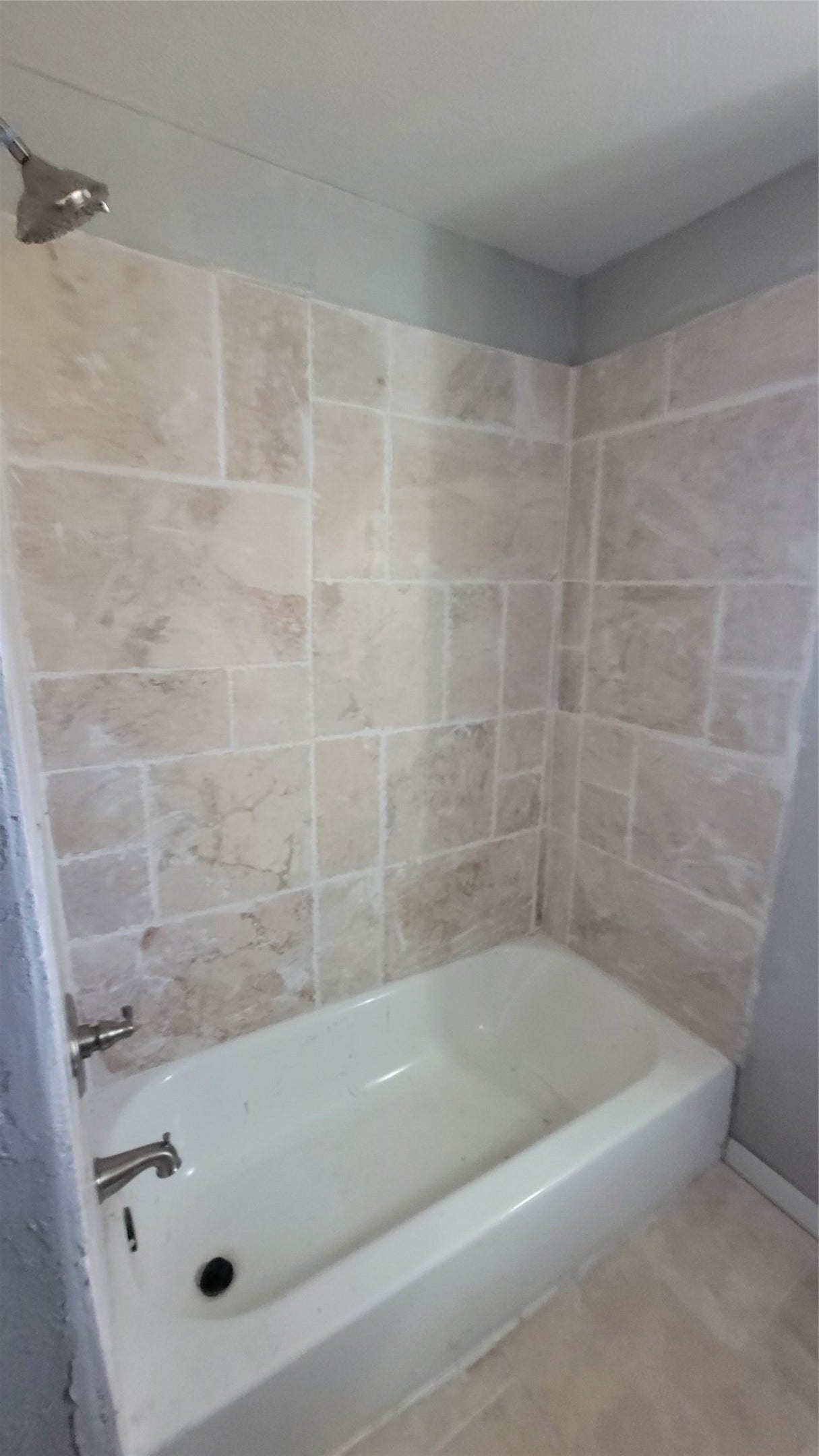 12018 Sandpiper Road, Angleton, TX 77515 This bathroom features a classic white bathtub with sleek fixtures, surrounded by beige tiled walls for a clean and neutral look.